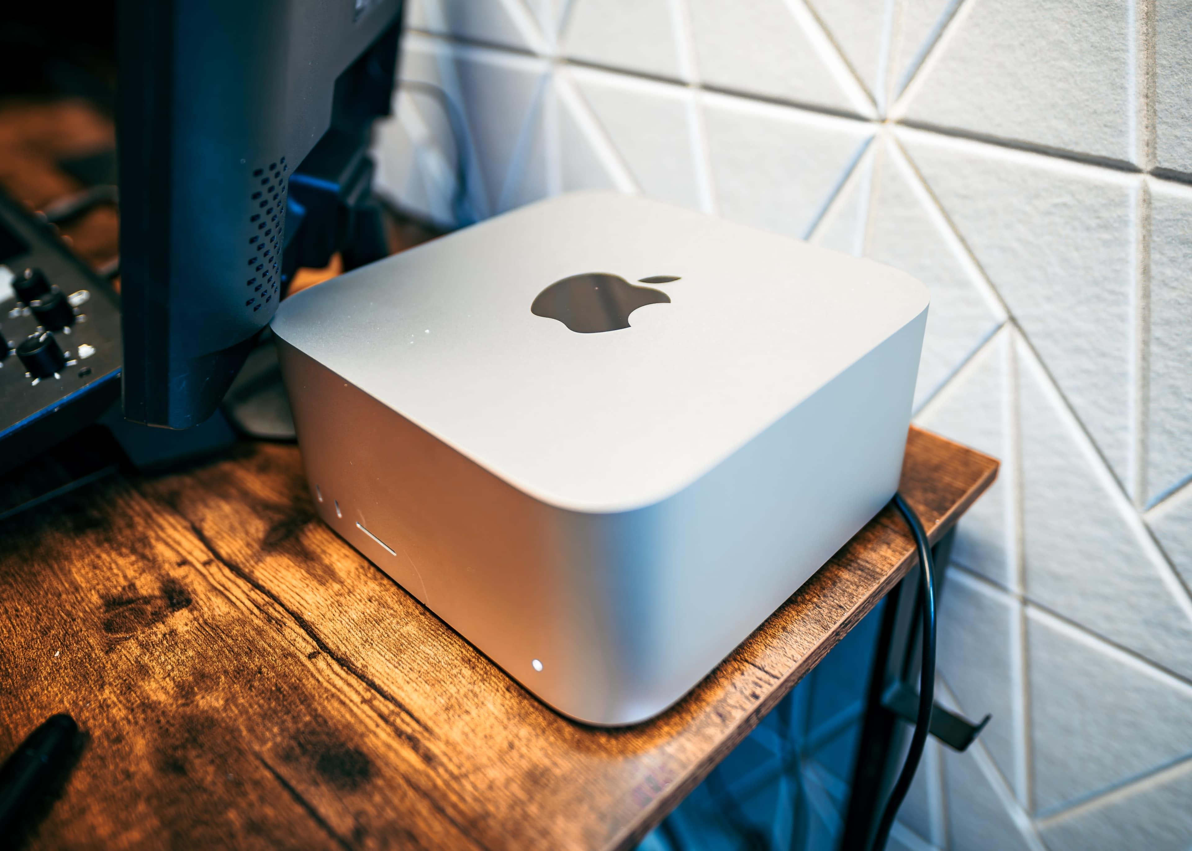 A sleek silver Apple computer is placed on a wooden desk beside a black monitor.