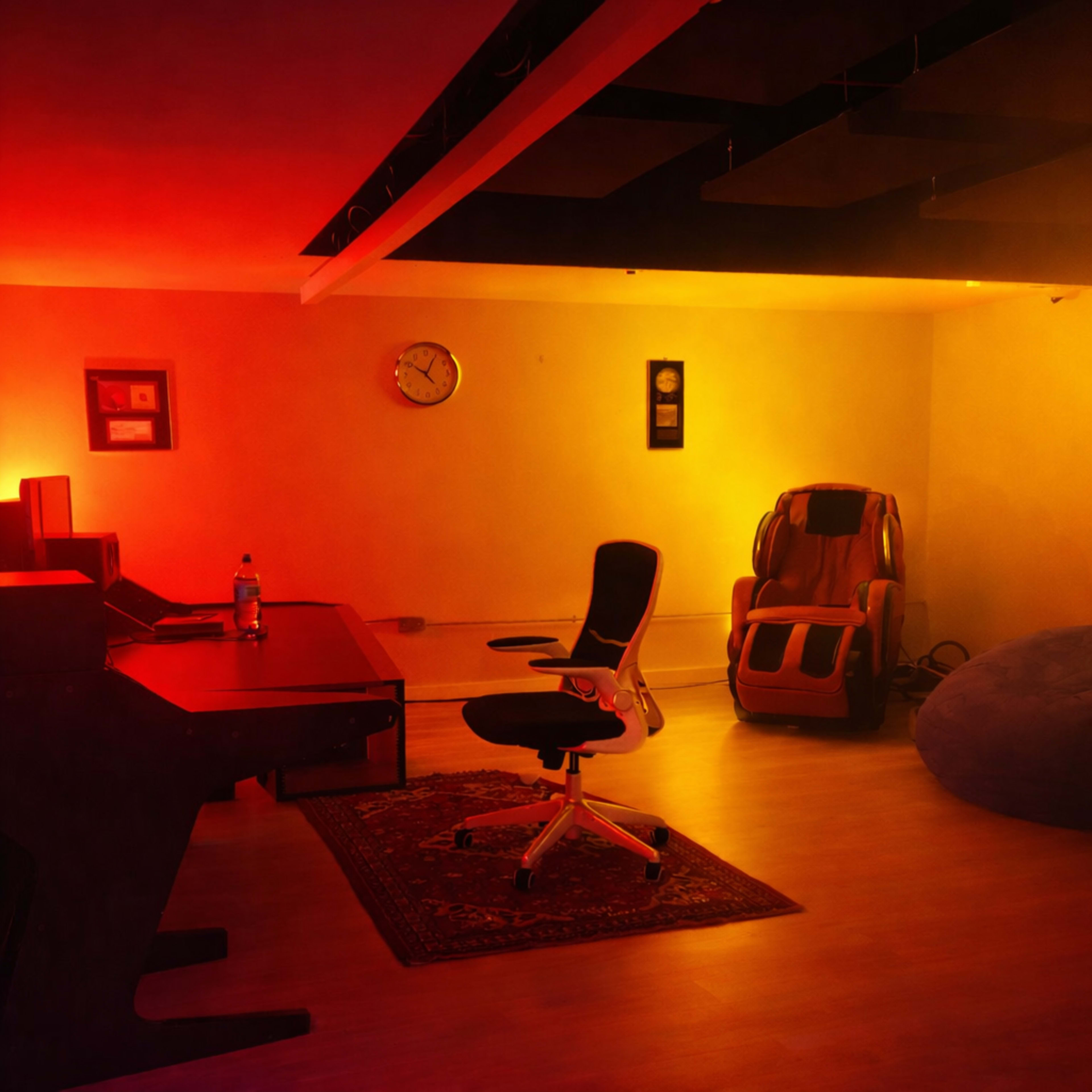 The image depicts a dimly lit room with a desk and chair, a massage chair, a bean bag, a clock on the wall, and ambient lighting.
