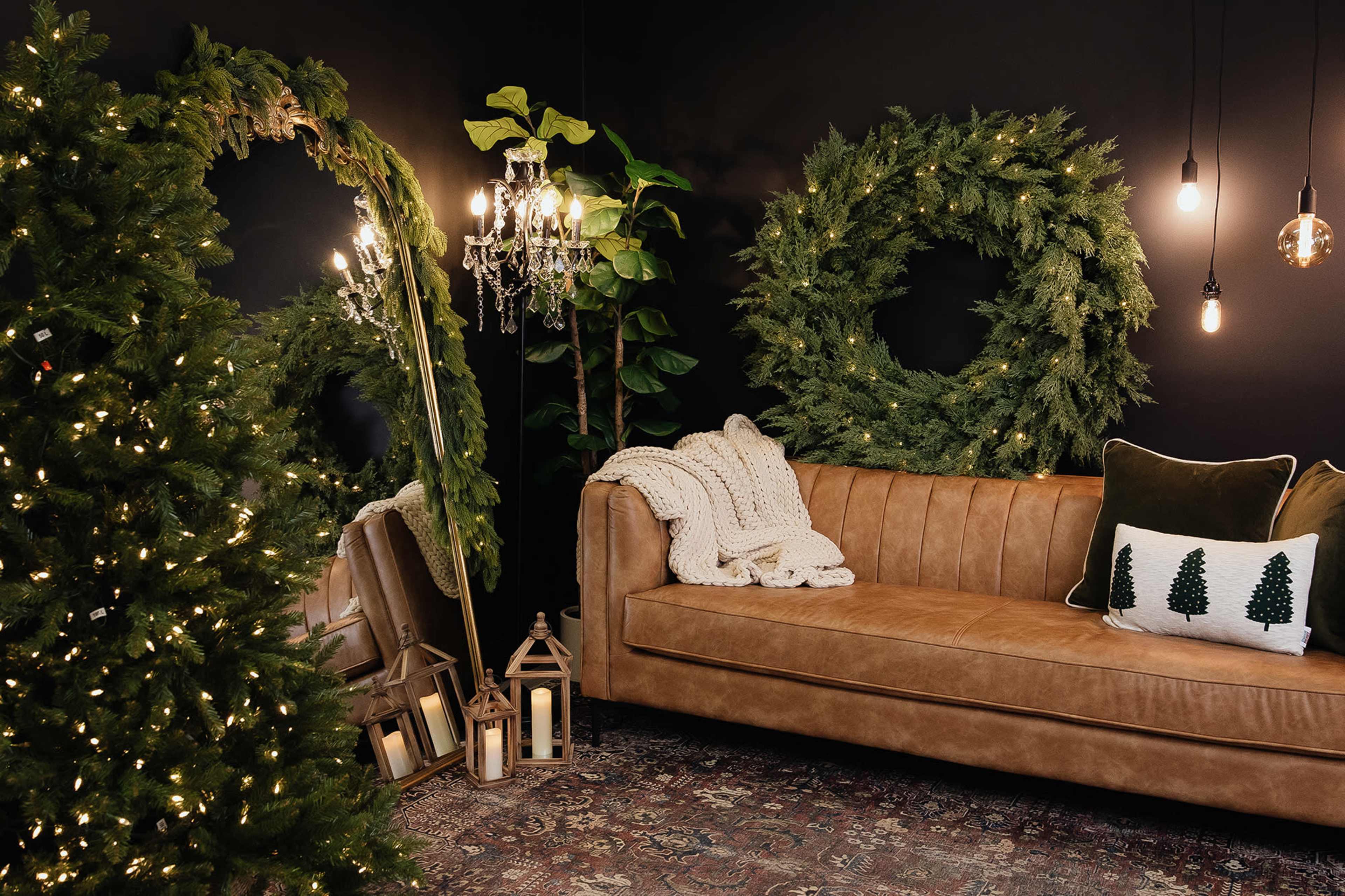 The scene features a cozy living room with a brown leather sofa, decorative wreaths on the walls, a Christmas tree, and warm lighting from hanging bulbs and a chandelier.