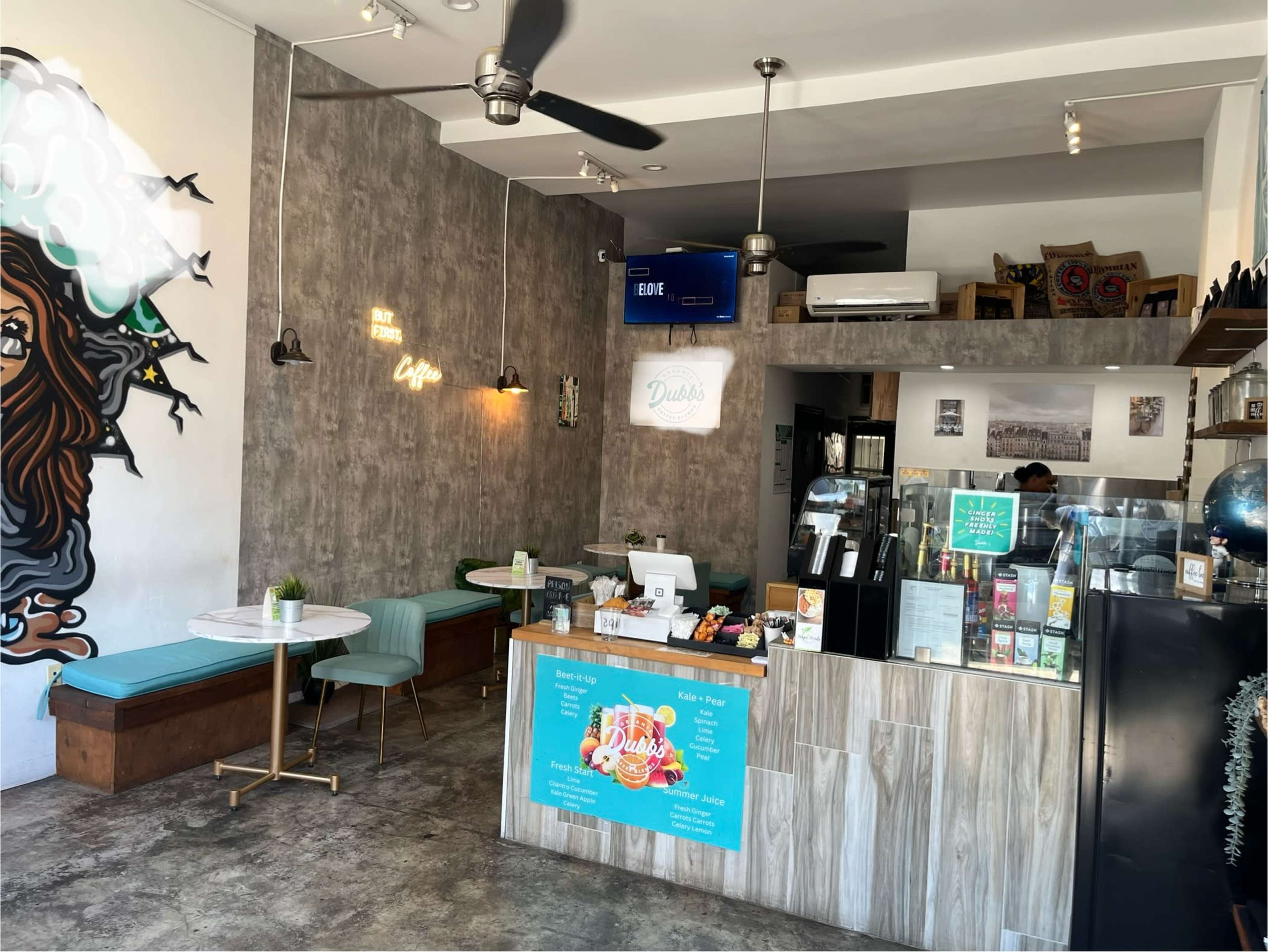 The interior of a cafe features a modern design with a service counter, seating area, and wall art.