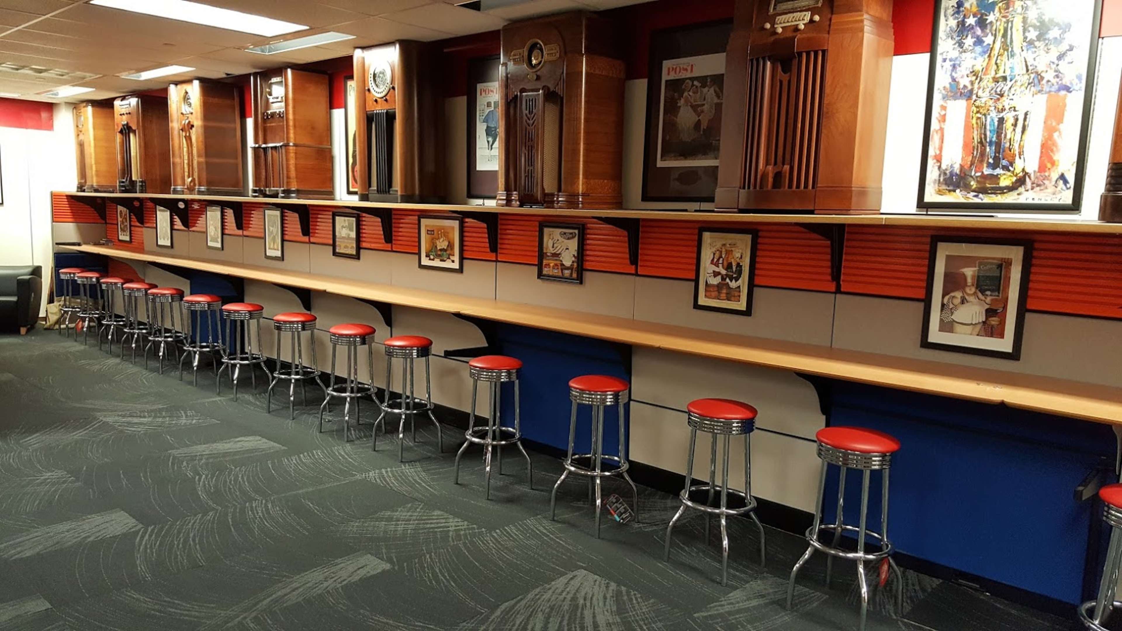A long counter with red-topped stools and wall-mounted photographs, flanked by tall wooden clock displays.