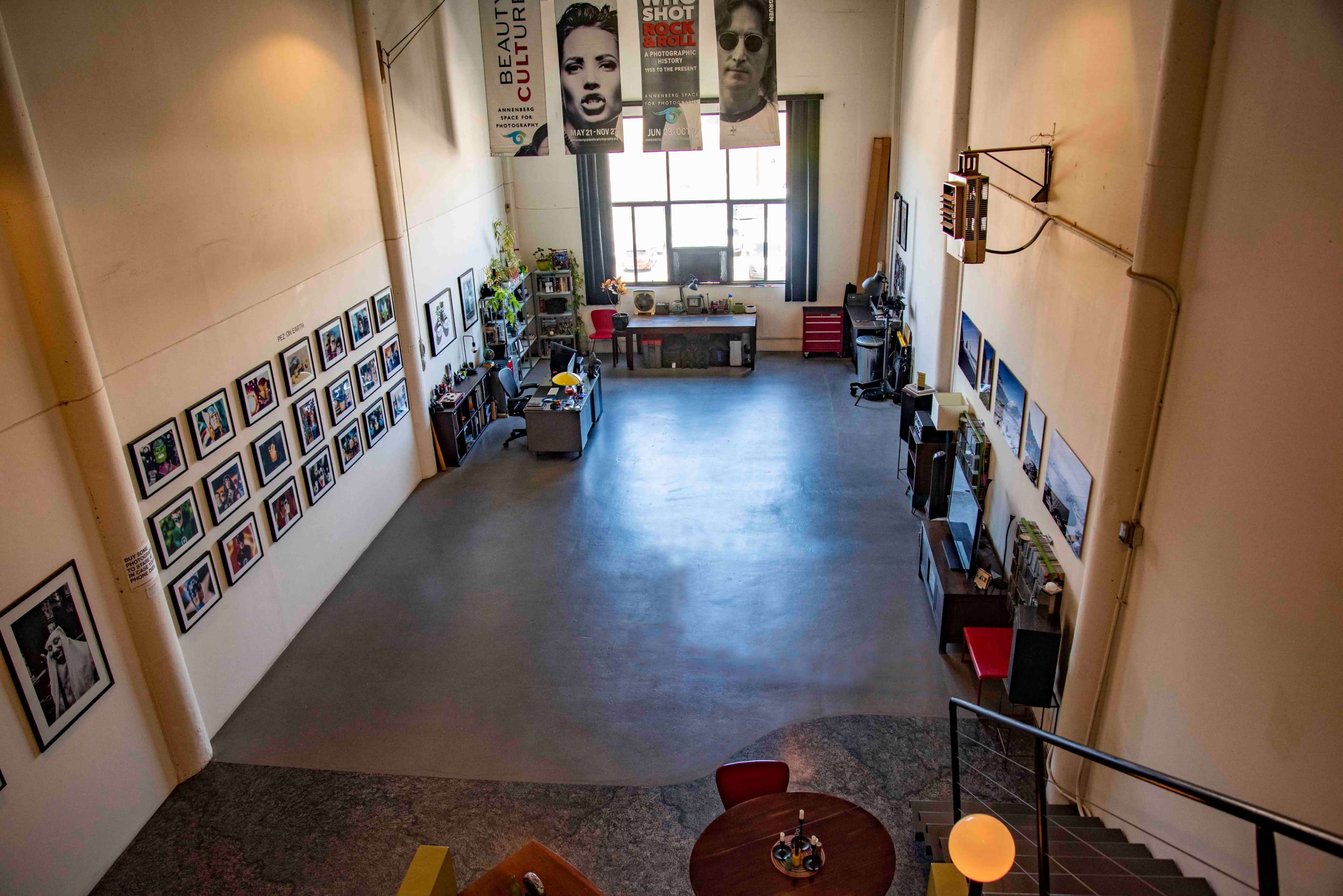A spacious art studio with a concrete floor, walls adorned with framed photographs, and various workstations along the sides.