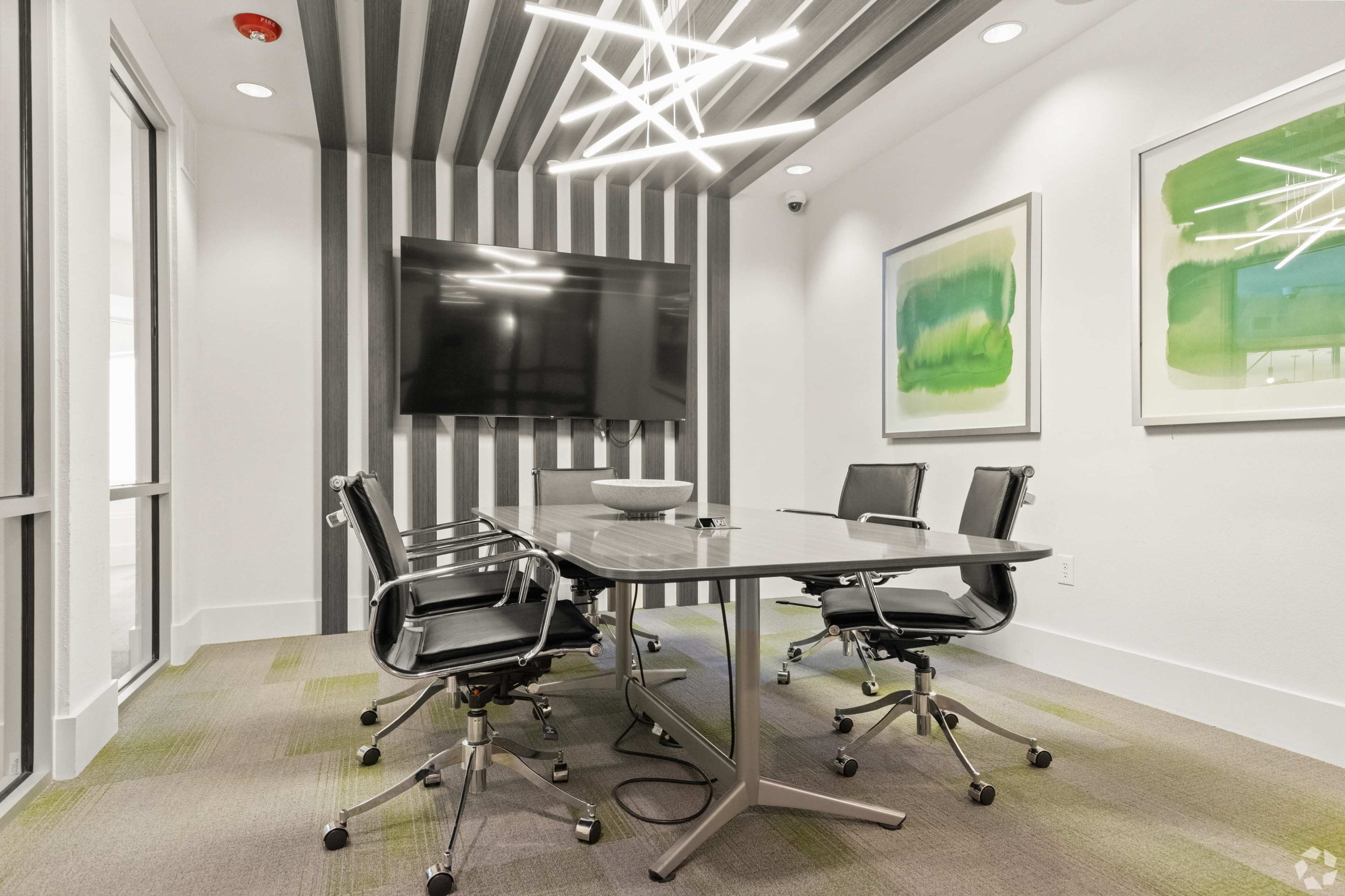 A modern conference room features a large table surrounded by black chairs, with a wall-mounted television and abstract artwork.