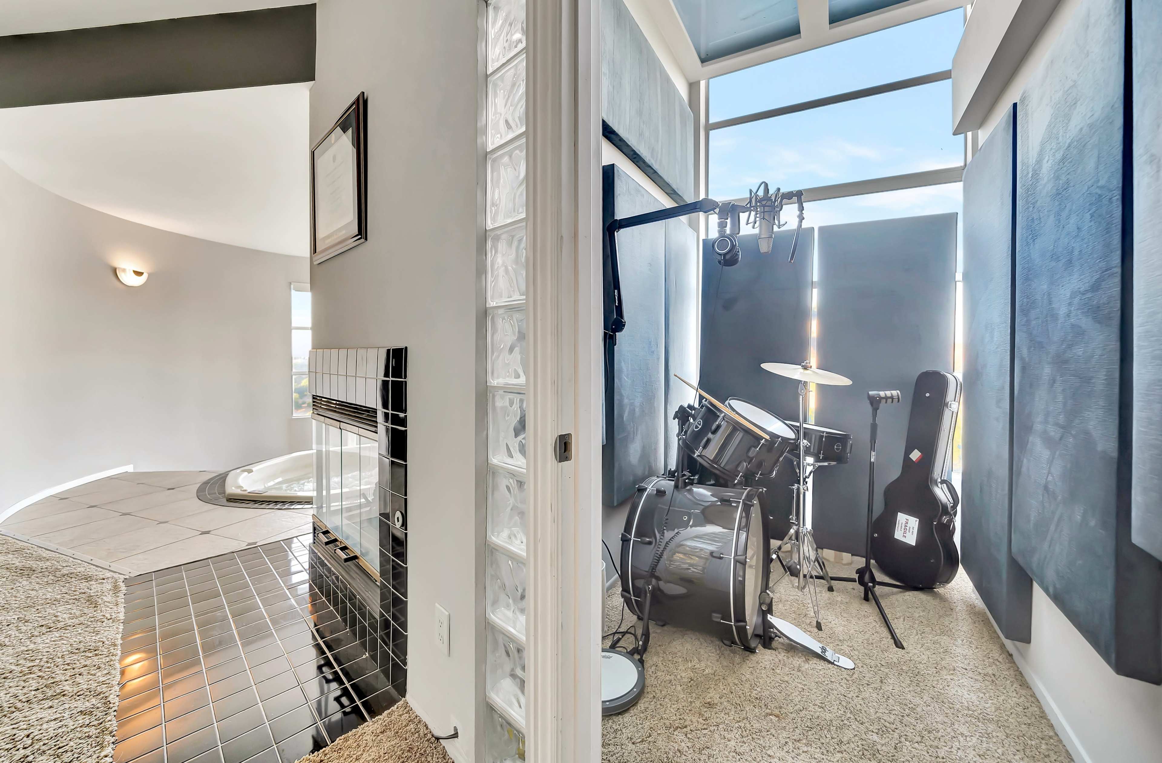 A corner of a room featuring a drum set and guitar beside a fireplace and a large window.