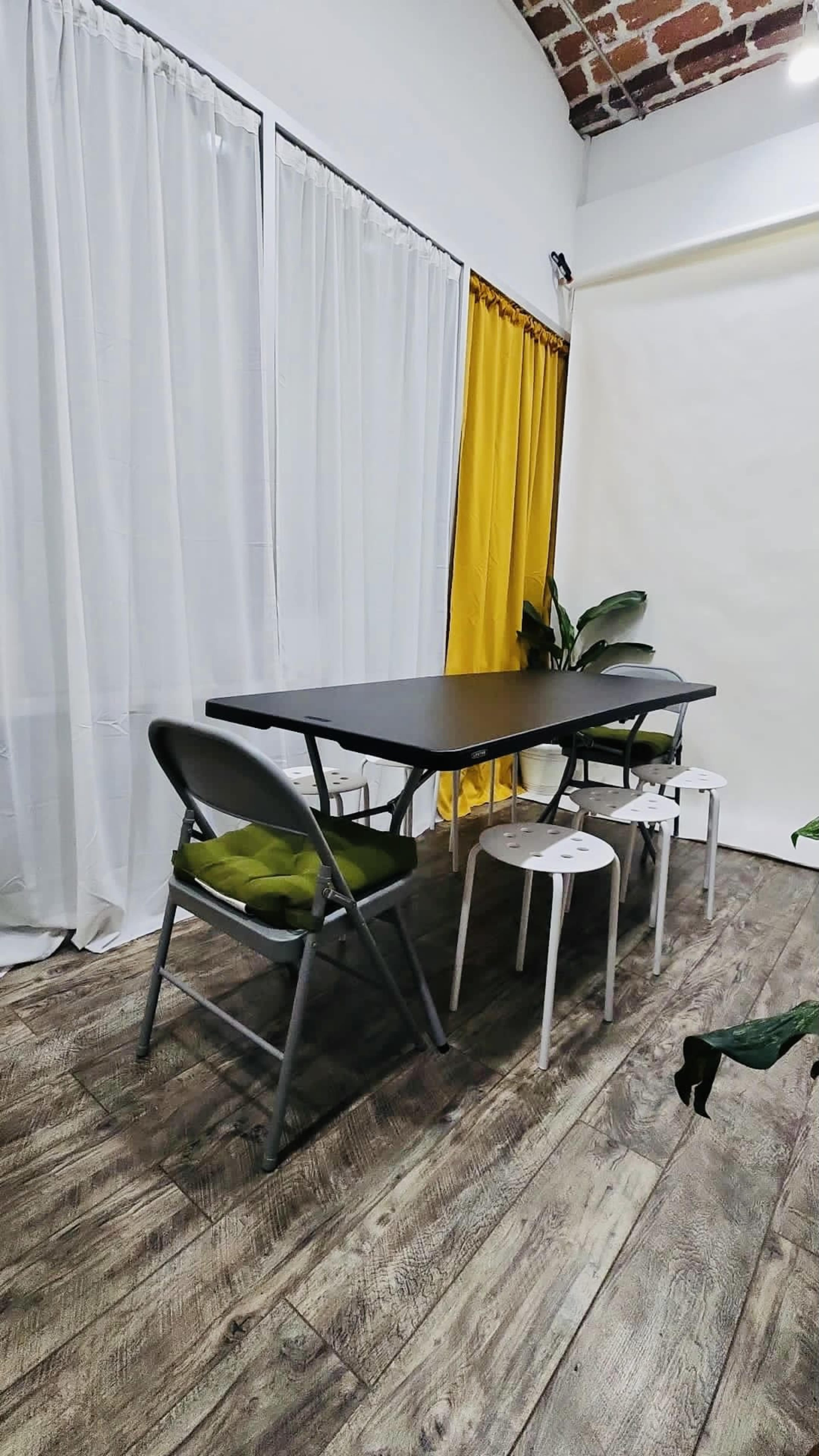 A black table stands in a room with wooden flooring, surrounded by three chairs and draped with white and yellow curtains.
