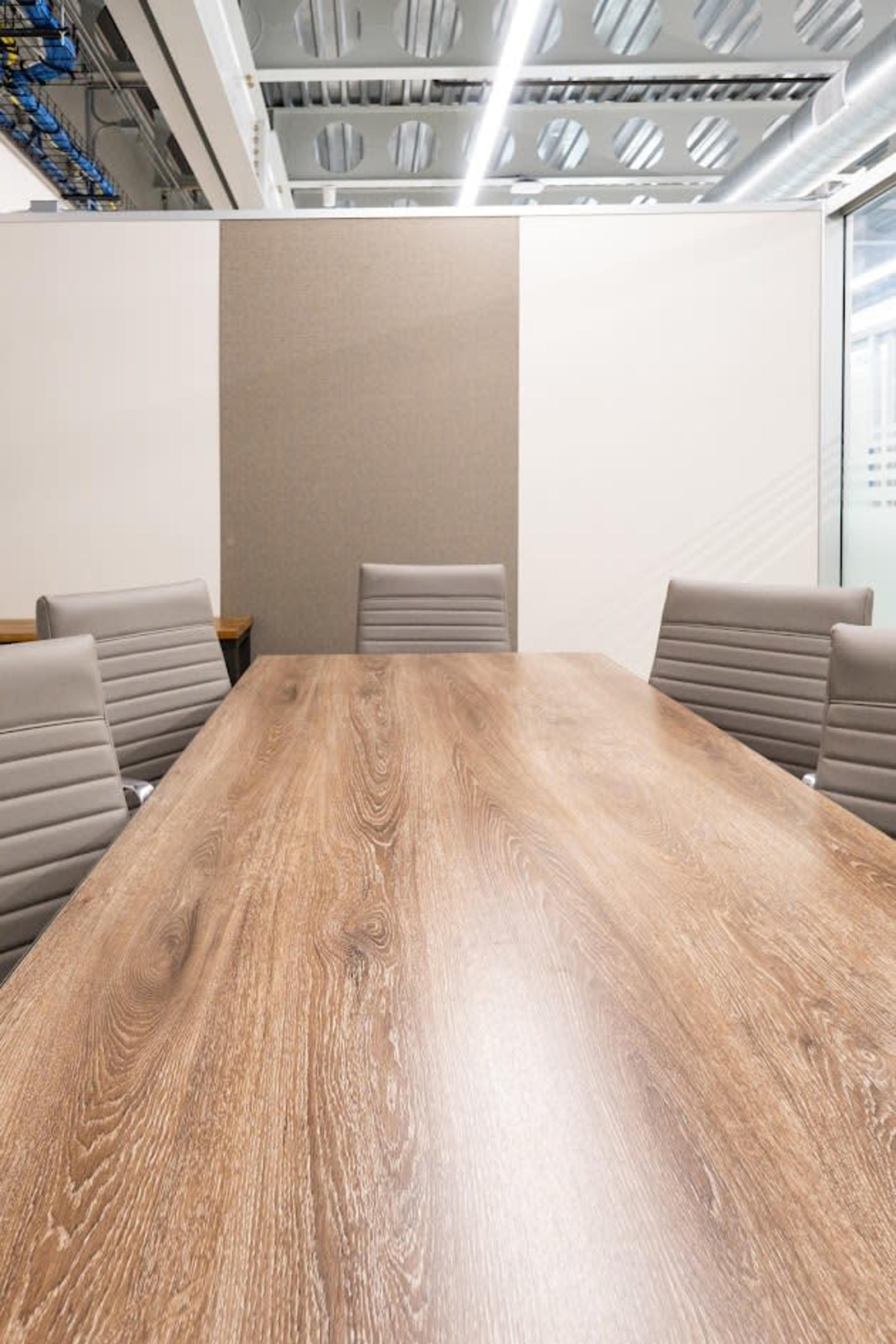 A long wooden conference table is surrounded by several gray chairs in a modern meeting room.