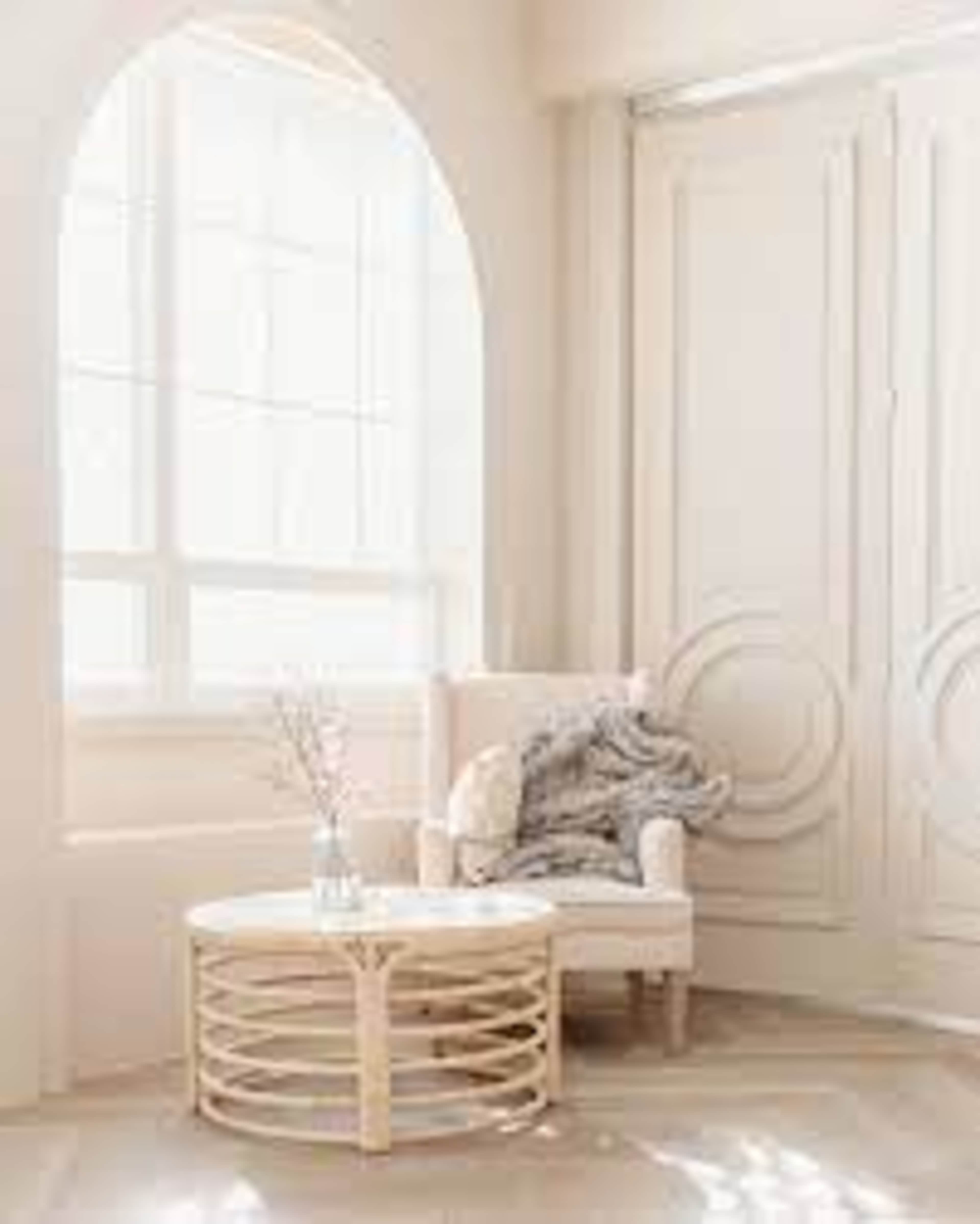 A cozy armchair is positioned beside a round coffee table in a sunlit room with tall windows and decorative doors.