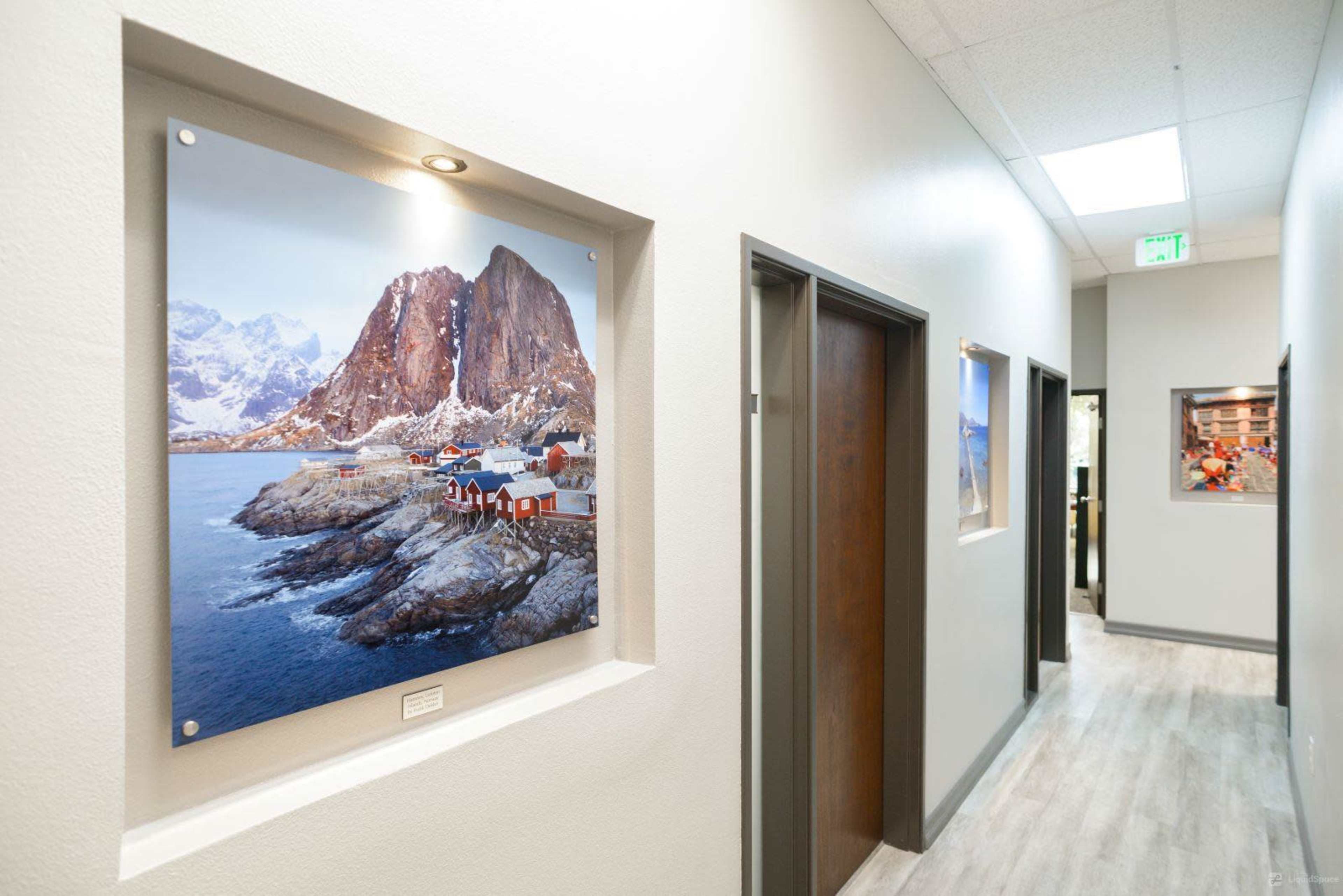 The image shows a hallway with framed photographs of coastal landscapes mounted on the walls and doors leading to rooms on either side.