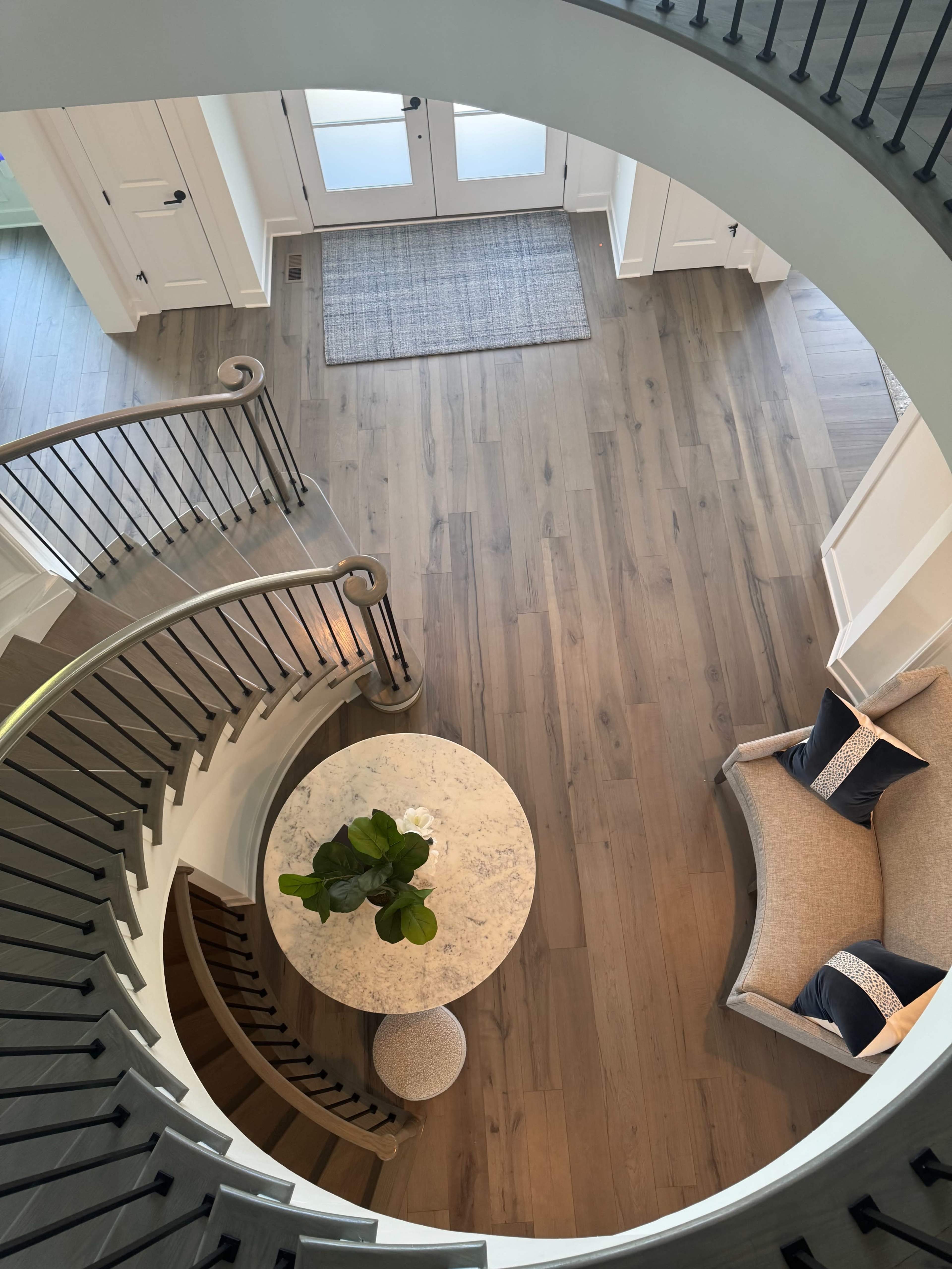 An aerial view of a circular staircase leading to a spacious foyer with a round table and a small seating area.