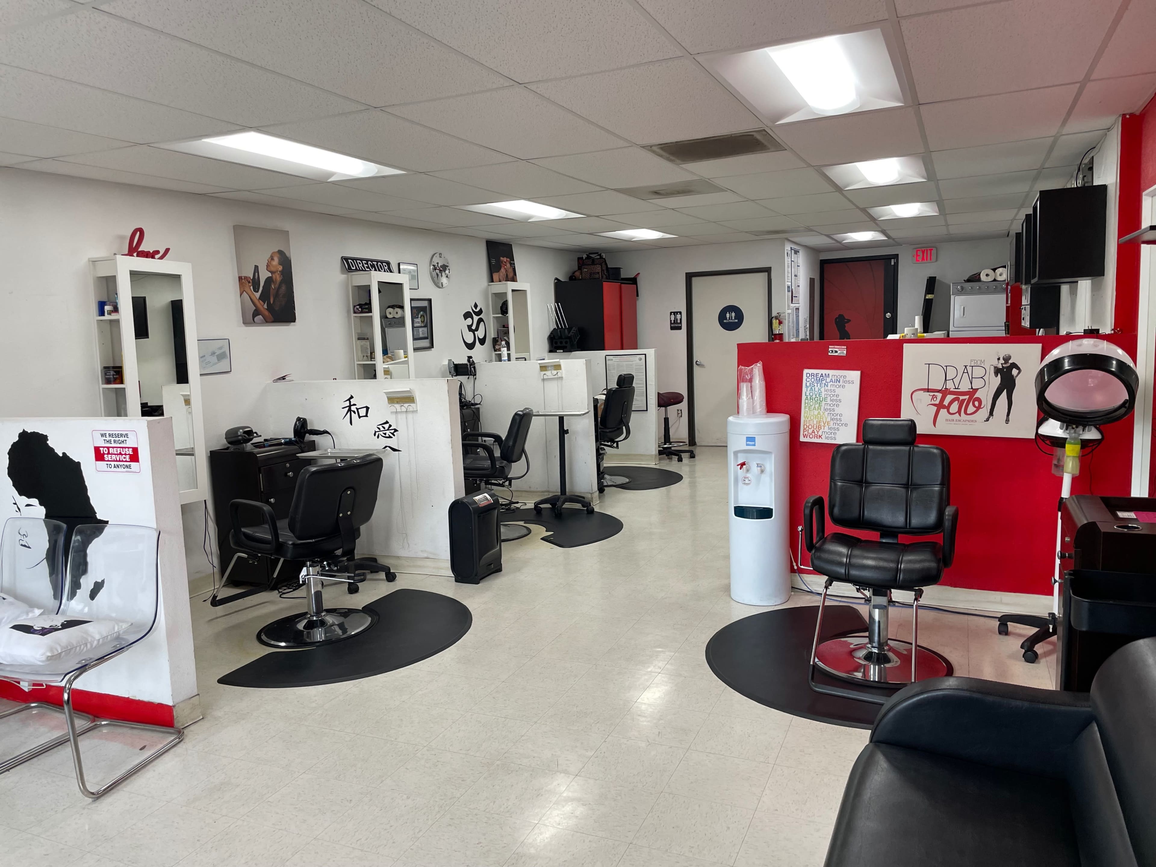 A spacious hair salon with several styling stations, black chairs, and red accent walls.