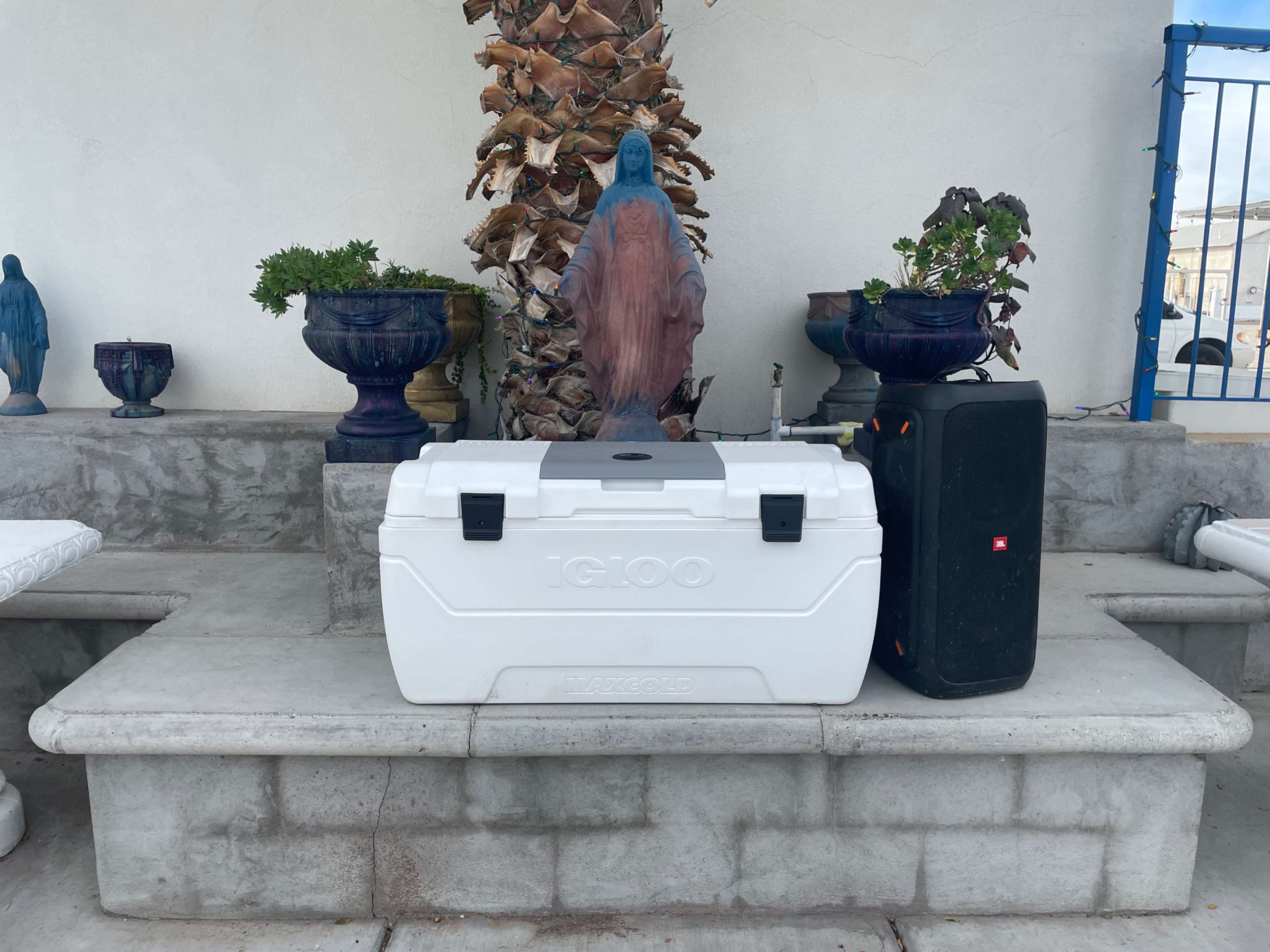 A white Igloo cooler and a black speaker are placed on a concrete bench next to a statue of a seated figure.