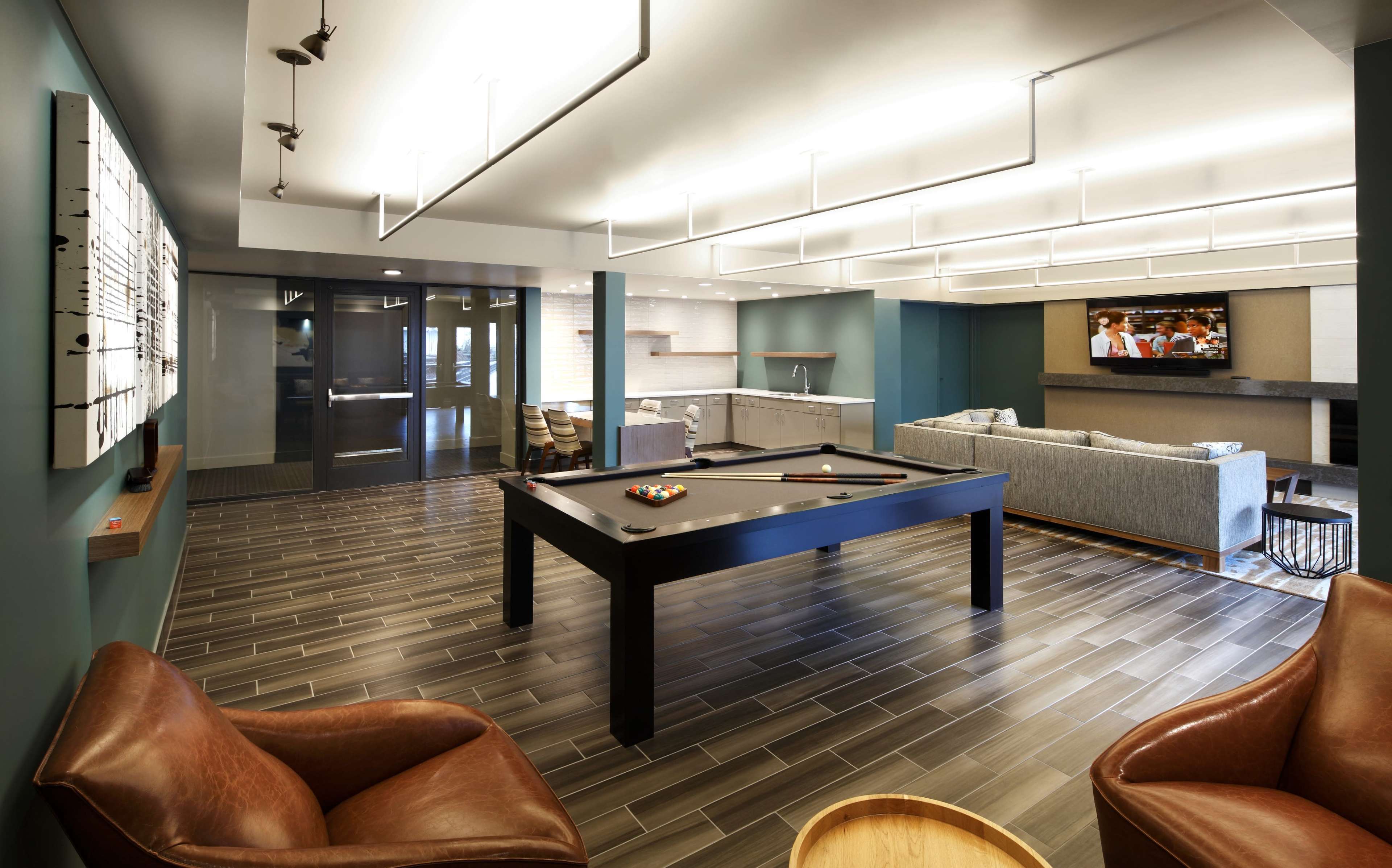 The image shows a modern recreational room featuring a pool table, comfortable seating, and a television mounted on the wall.