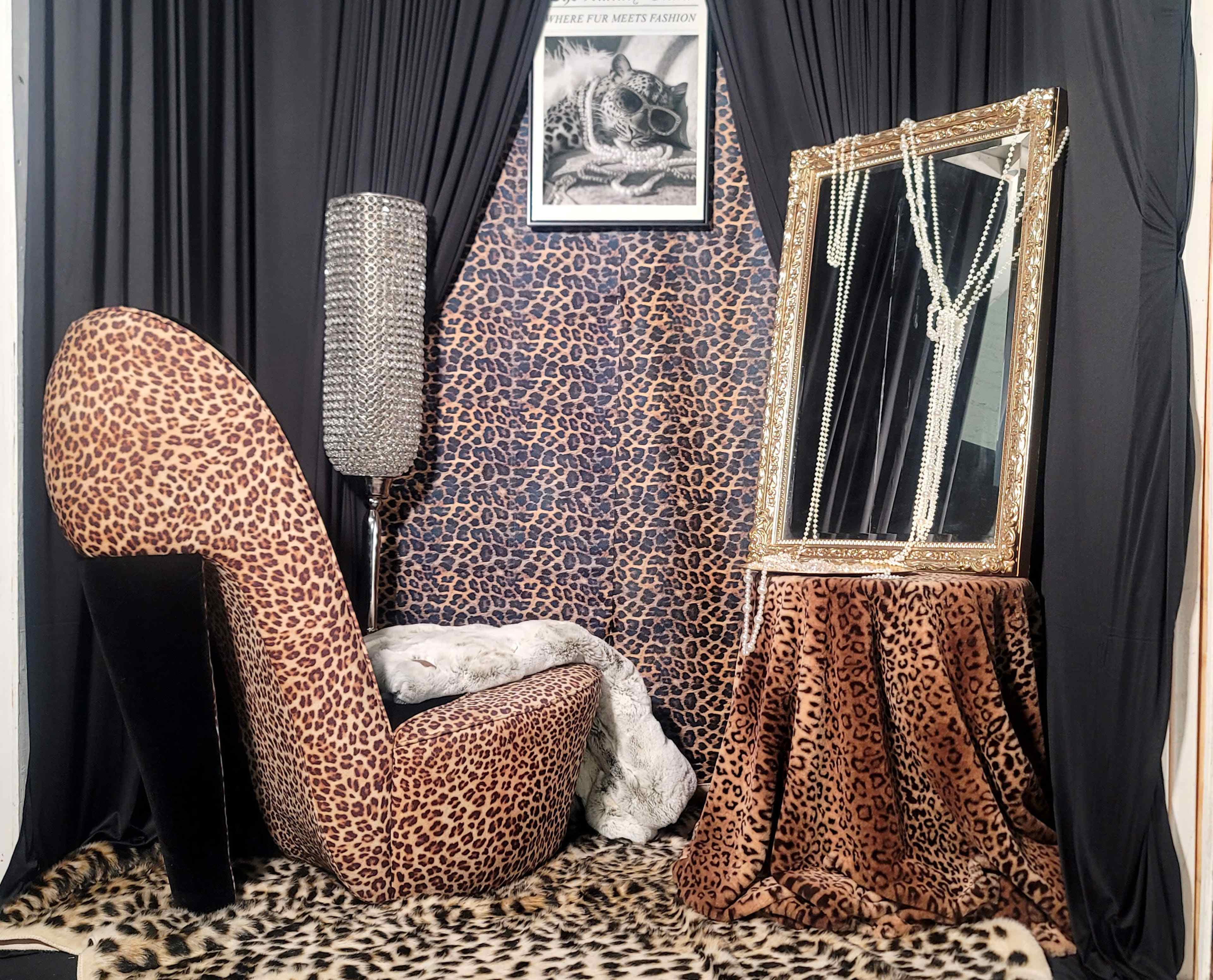 The scene features a stylish corner with a leopard print chair, a table draped in leopard fabric, and a large mirror framed in gold, all set against a backdrop of black curtains and a patterned wall.