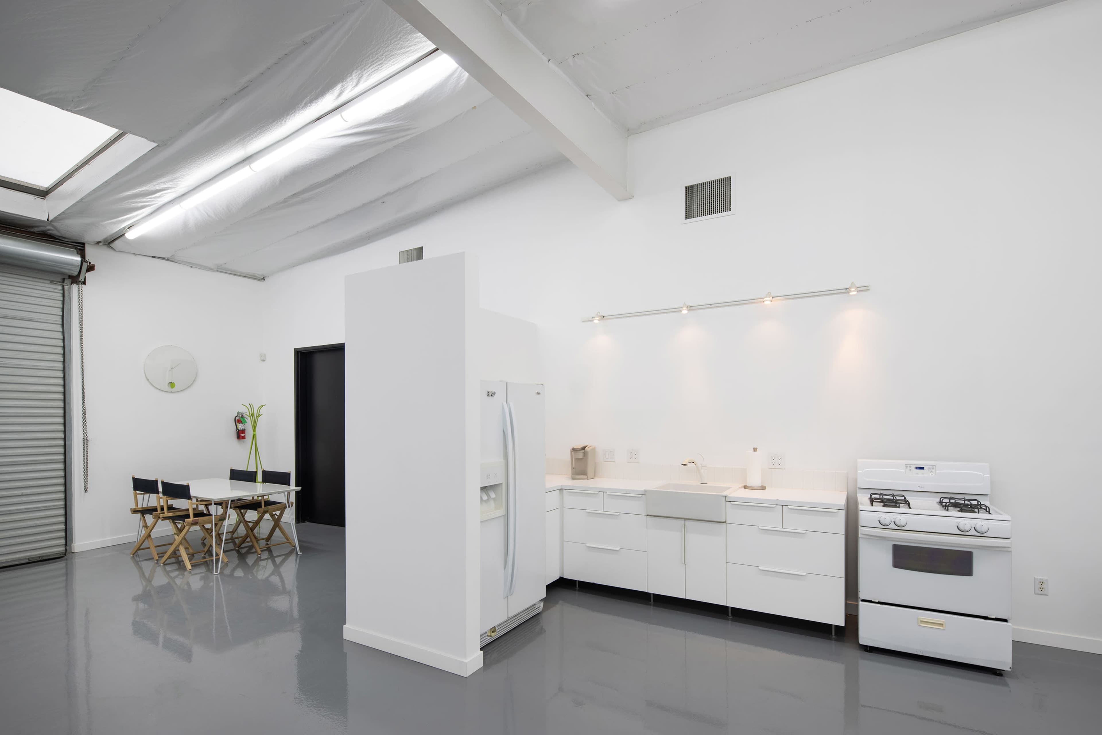 A minimalist kitchen area with white cabinetry, a stove, a refrigerator, and a dining table with two chairs.
