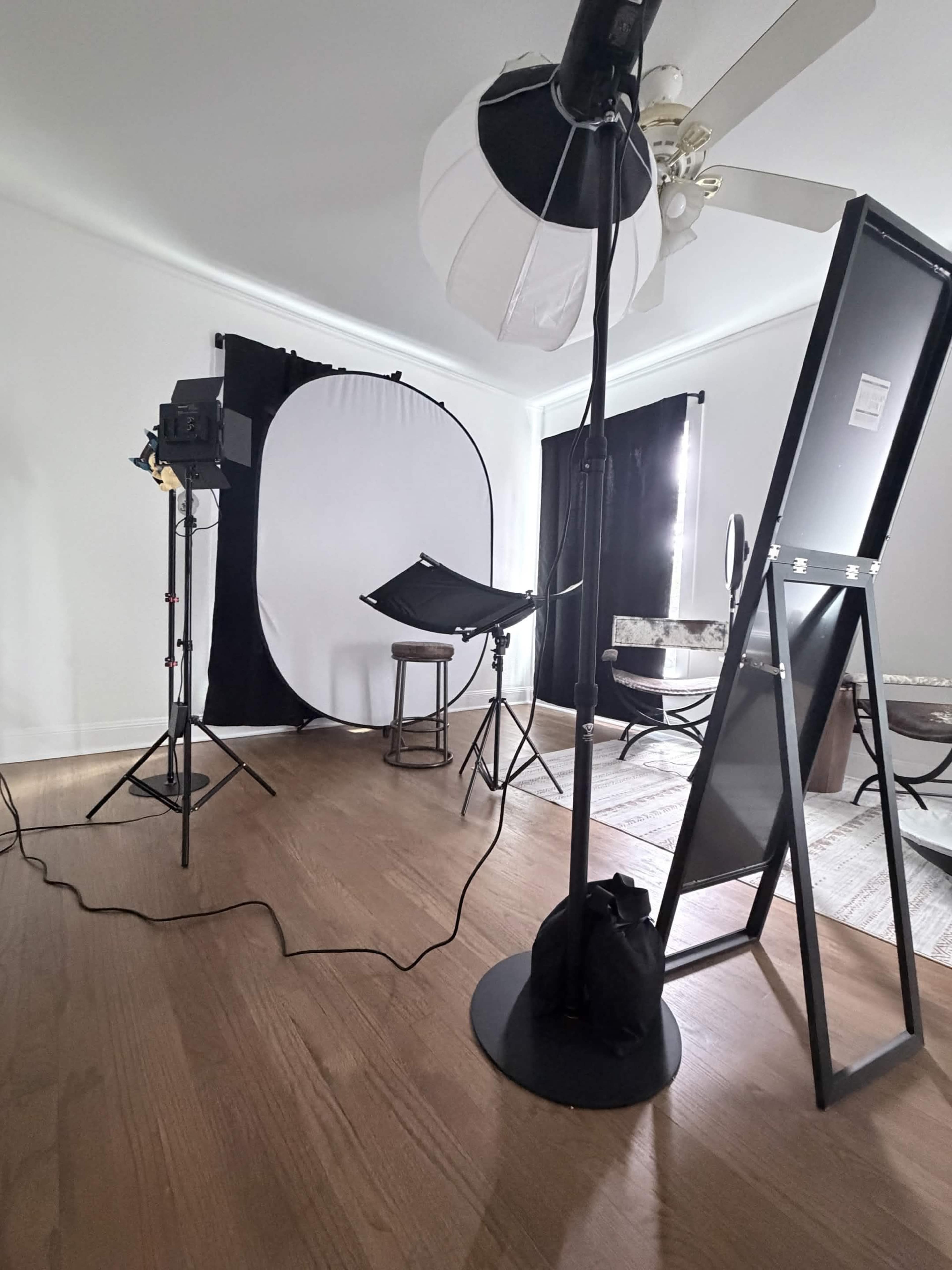 The image shows a photography studio setup with lighting equipment, a backdrop, and a stool placed on a wooden floor.