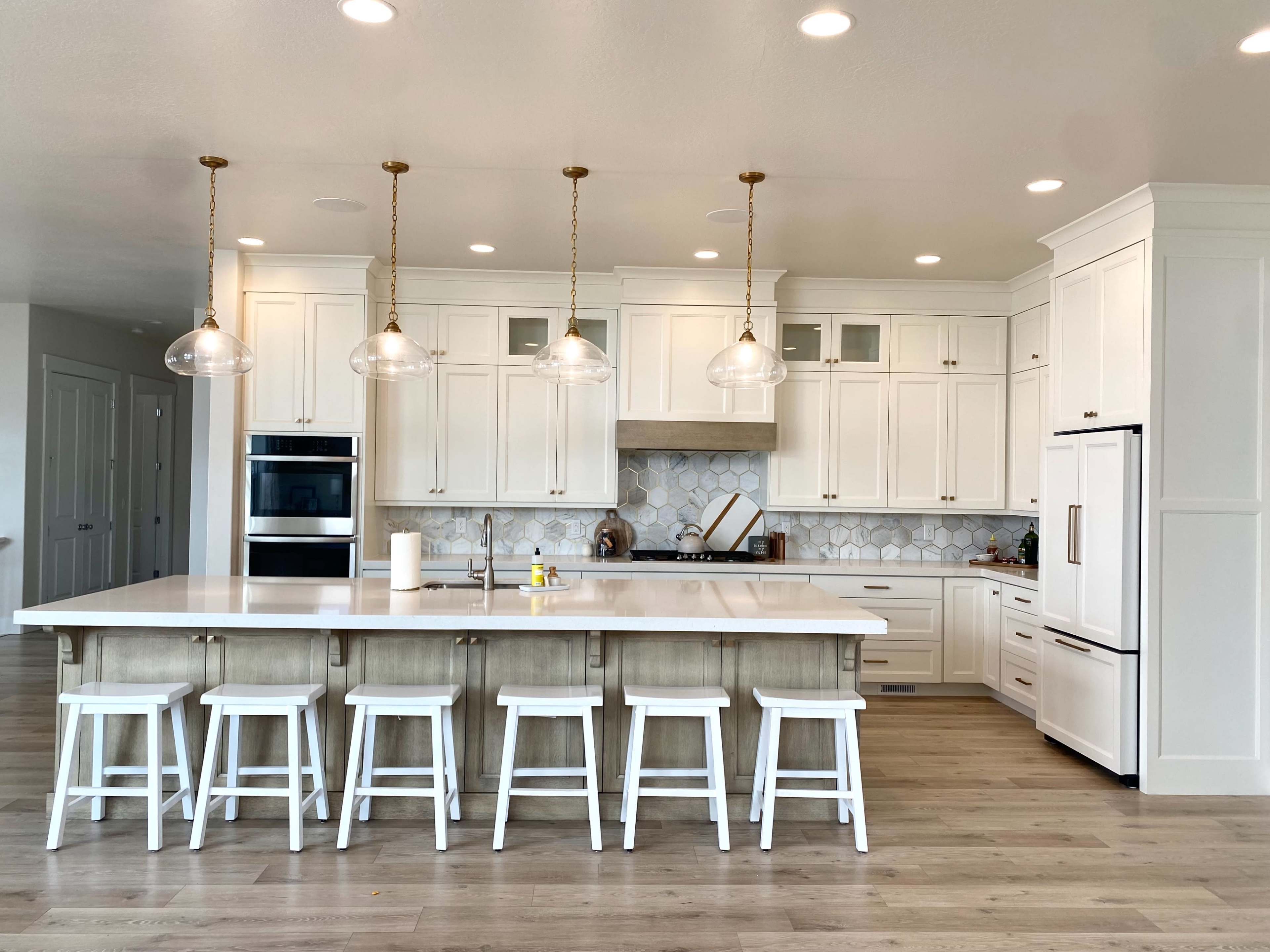 A modern kitchen features white cabinetry, a large island with seating for six, and pendant lights hanging above.