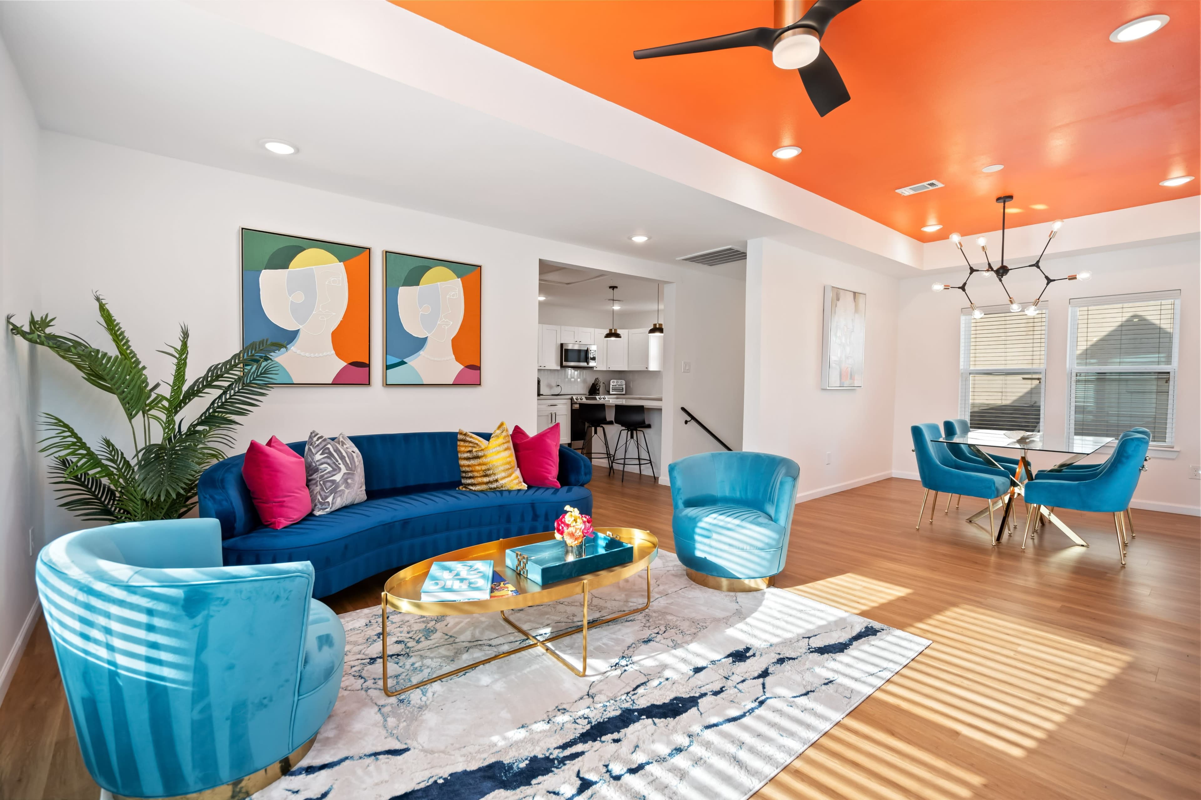The living room features a blue sectional sofa, bright orange ceiling, and modern furniture arranged around a circular coffee table.
