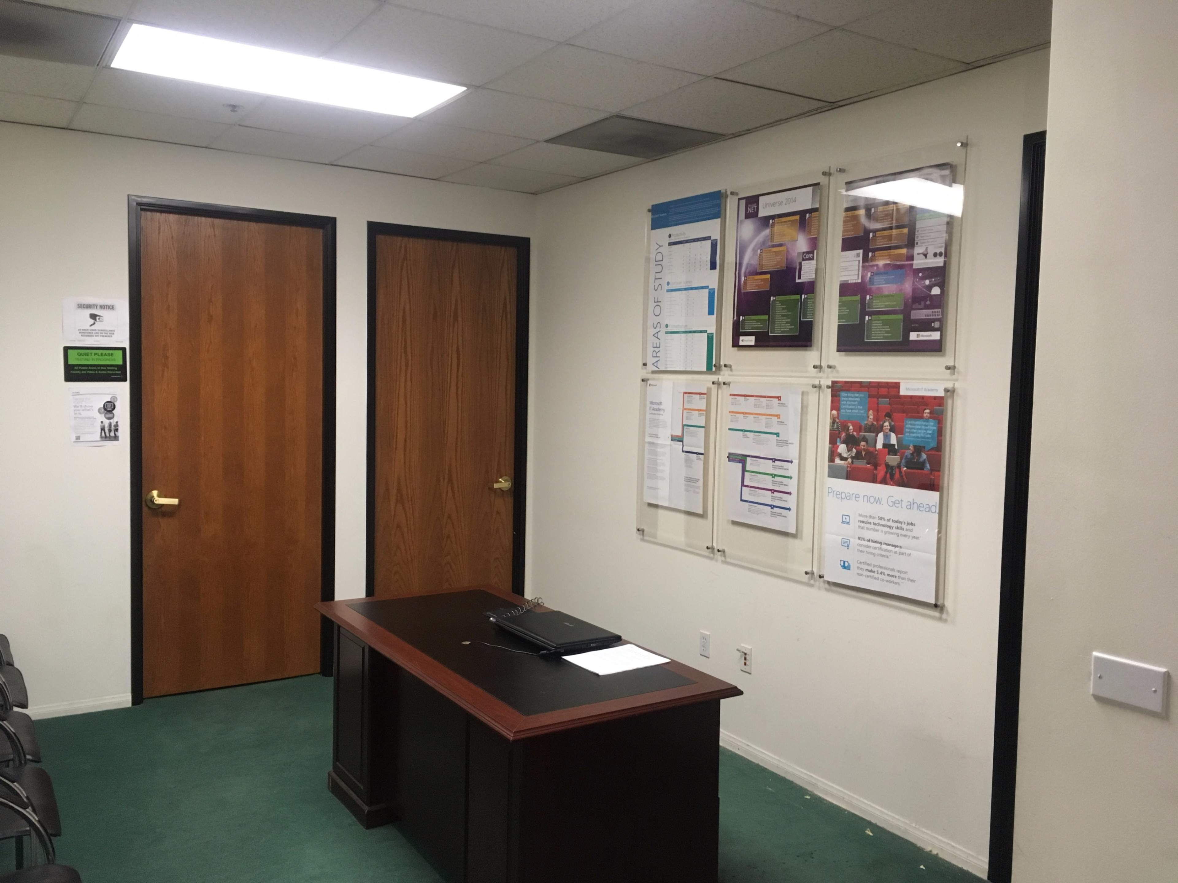 A small office space with two closed wooden doors, a wooden desk, and information posters mounted on the wall.