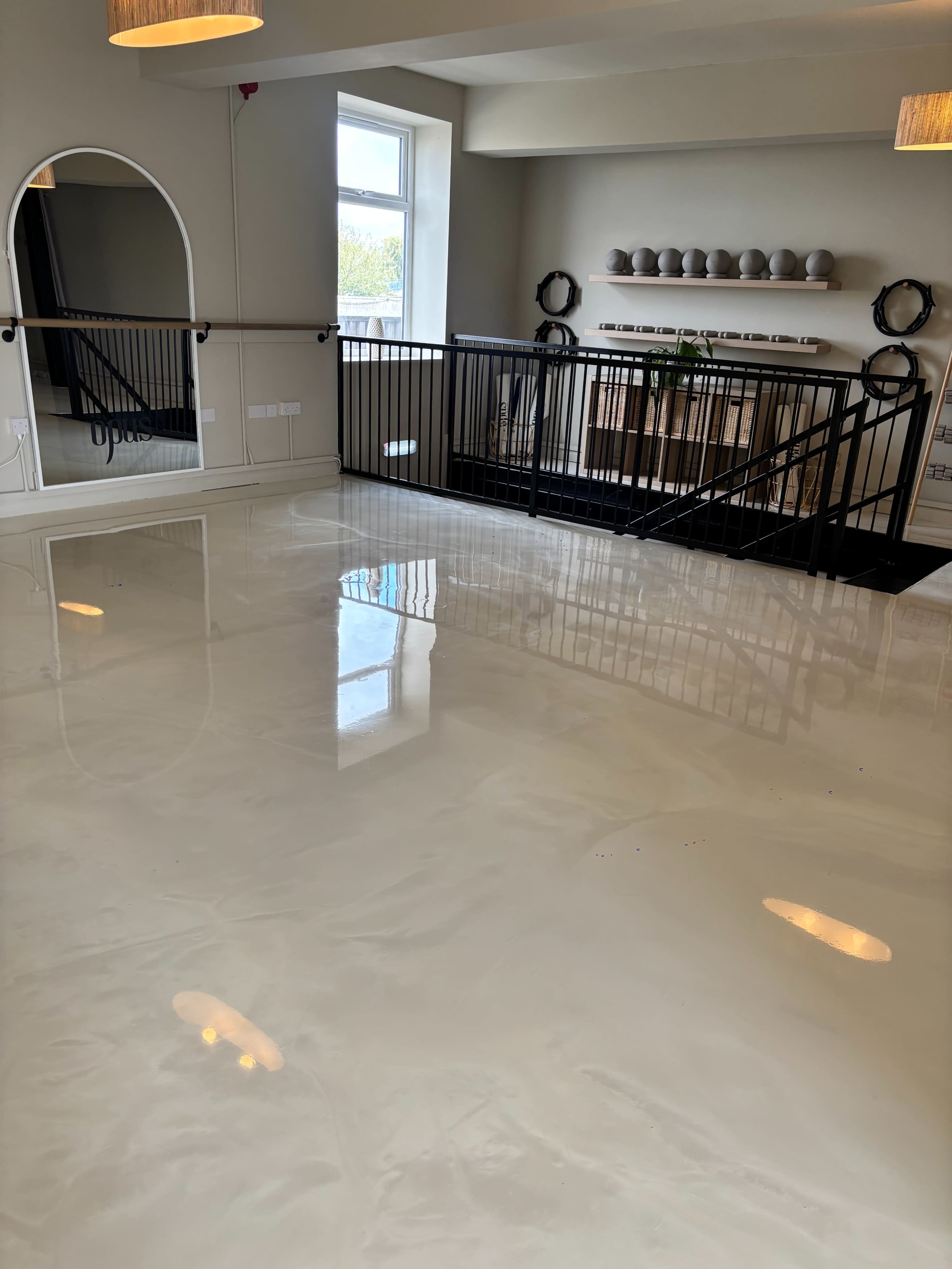The image shows a well-lit interior space with a glossy, polished floor, a stylish railing, and decorative objects on a shelf in the background.