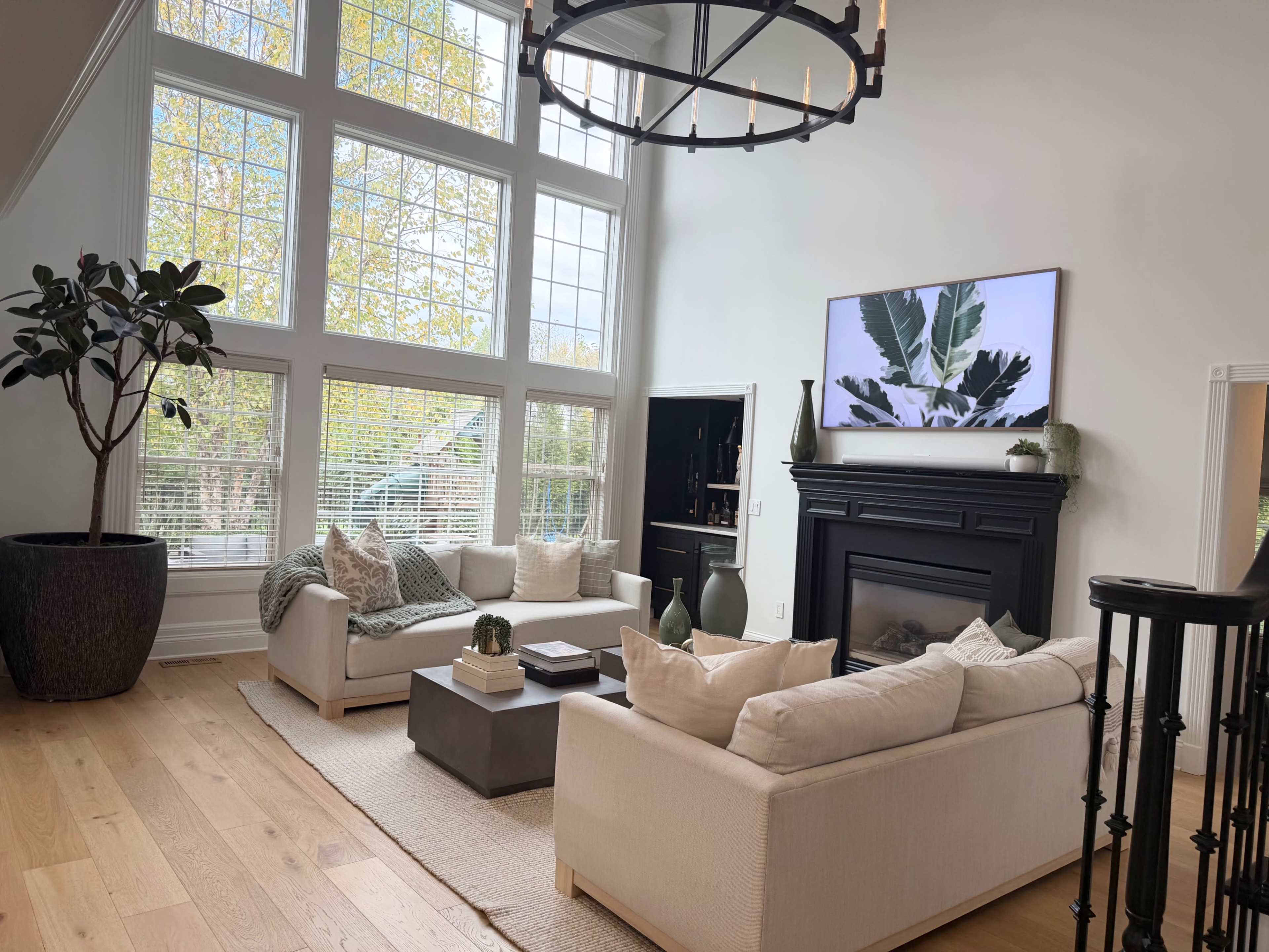 The living room features large windows, a black fireplace, and two cream-colored sofas arranged around a coffee table.