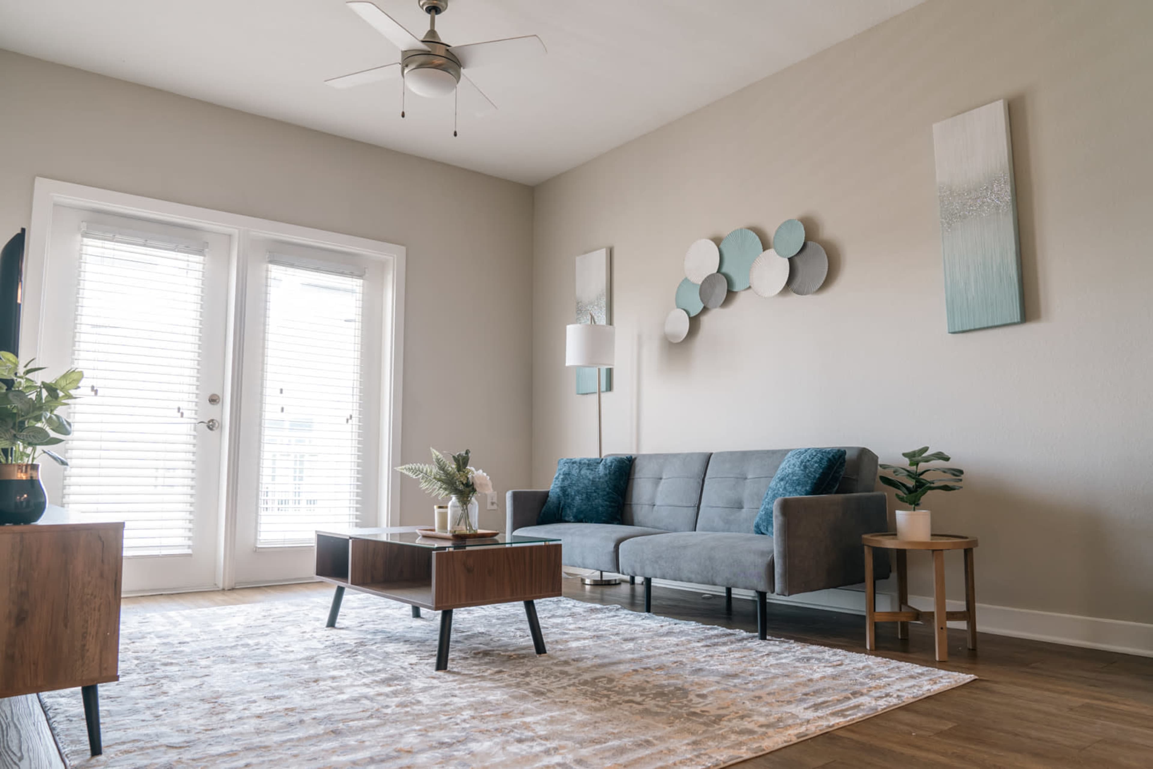 The living room features a gray sofa, a wooden coffee table, and a large area rug with light-colored walls and sliding glass doors.