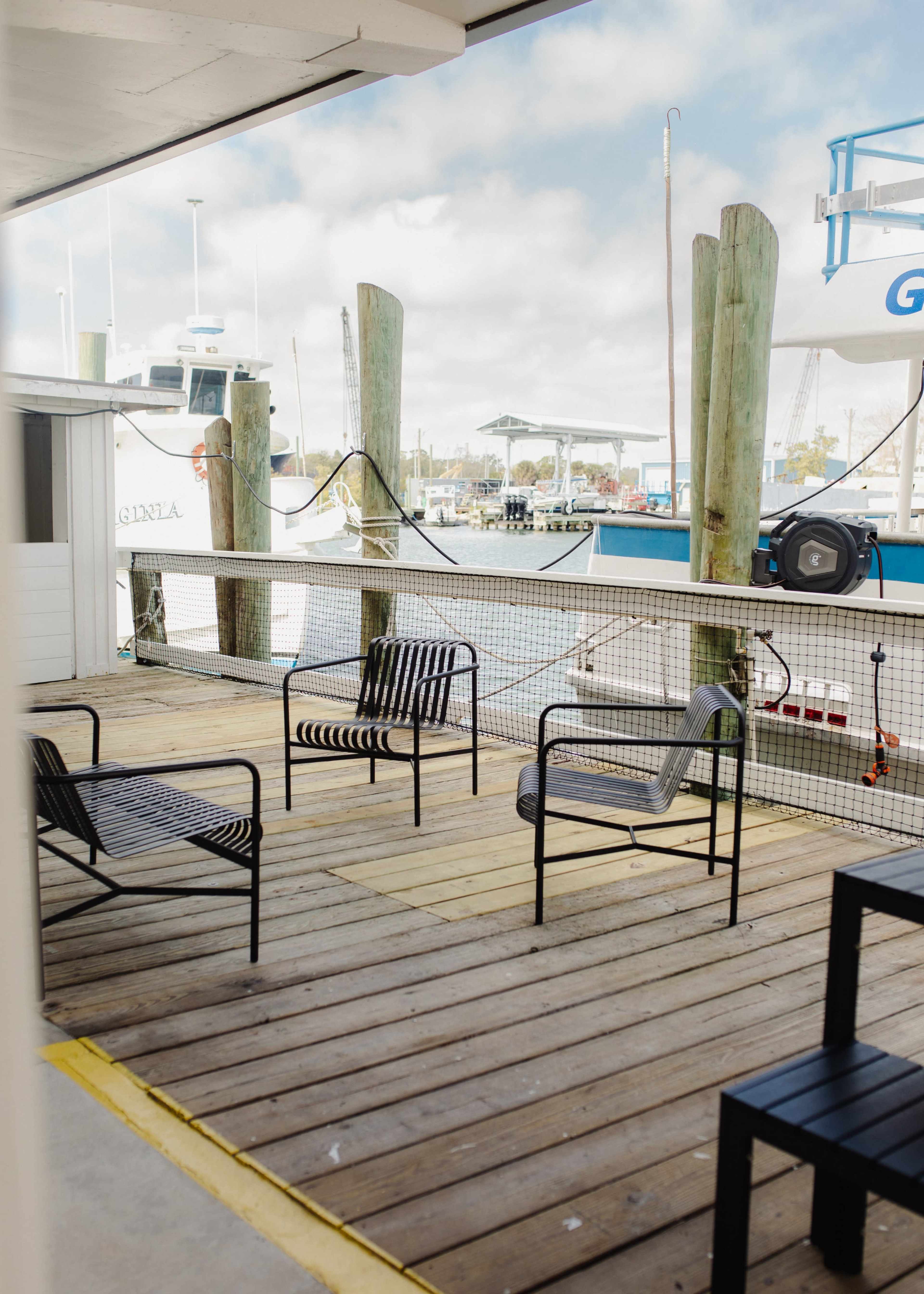 The image shows a wooden dock area with several black and white striped chairs facing a marina where boats are moored.