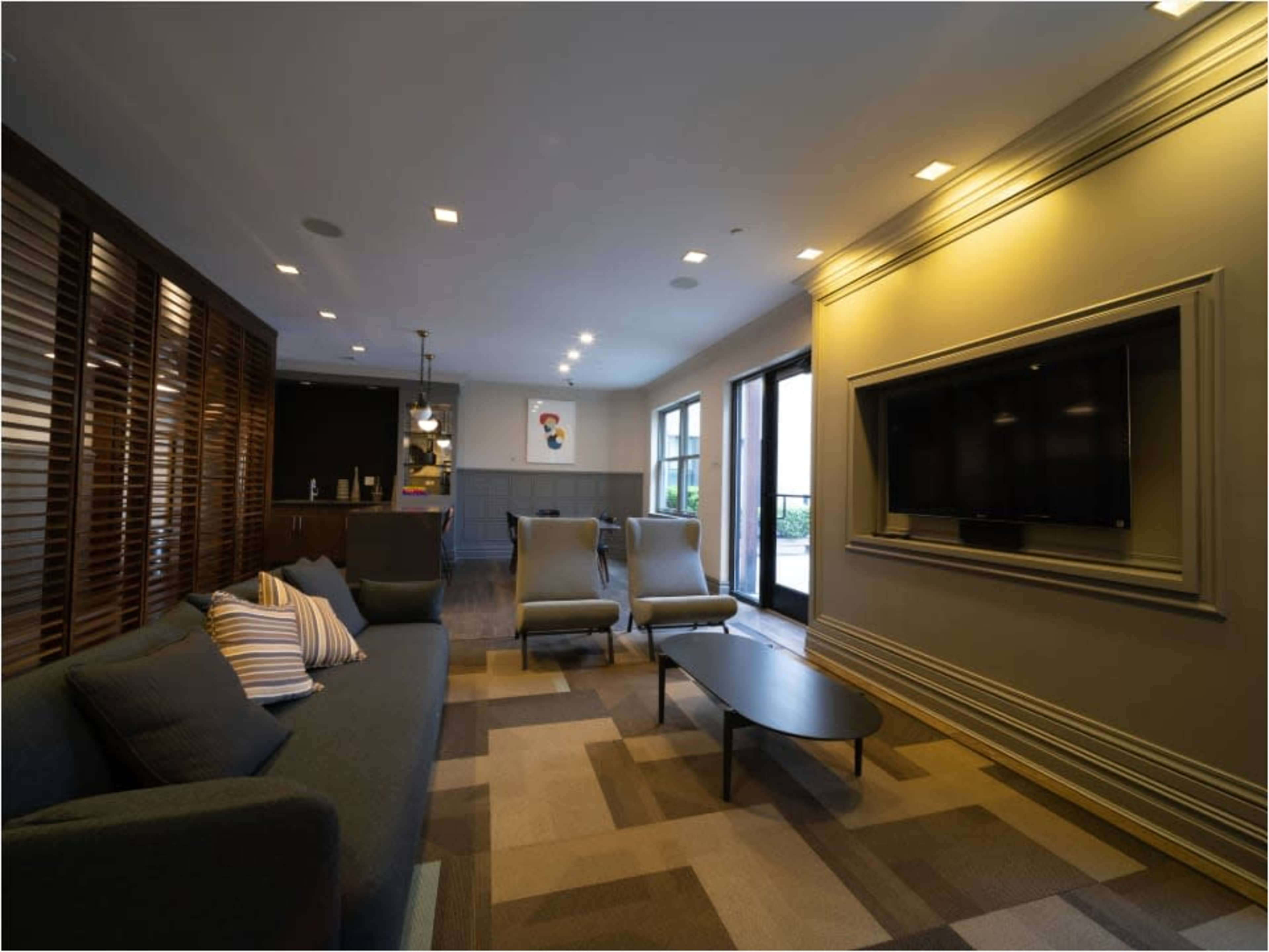 The image shows a modern lounge area with a sofa, two chairs, a coffee table, and a wall-mounted television.