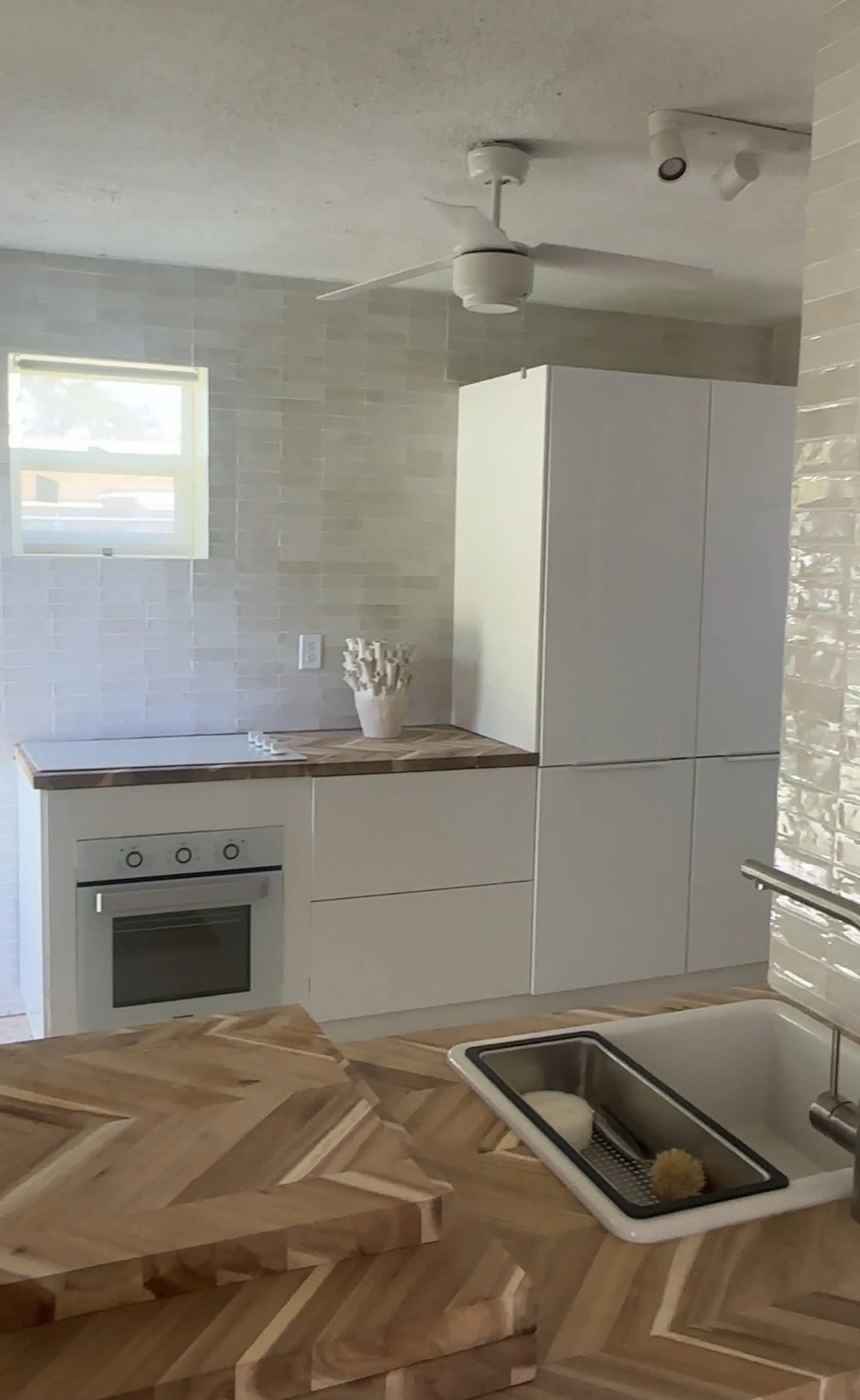 A modern kitchen with a white refrigerator, a built-in oven, and a sink on a wooden countertop.