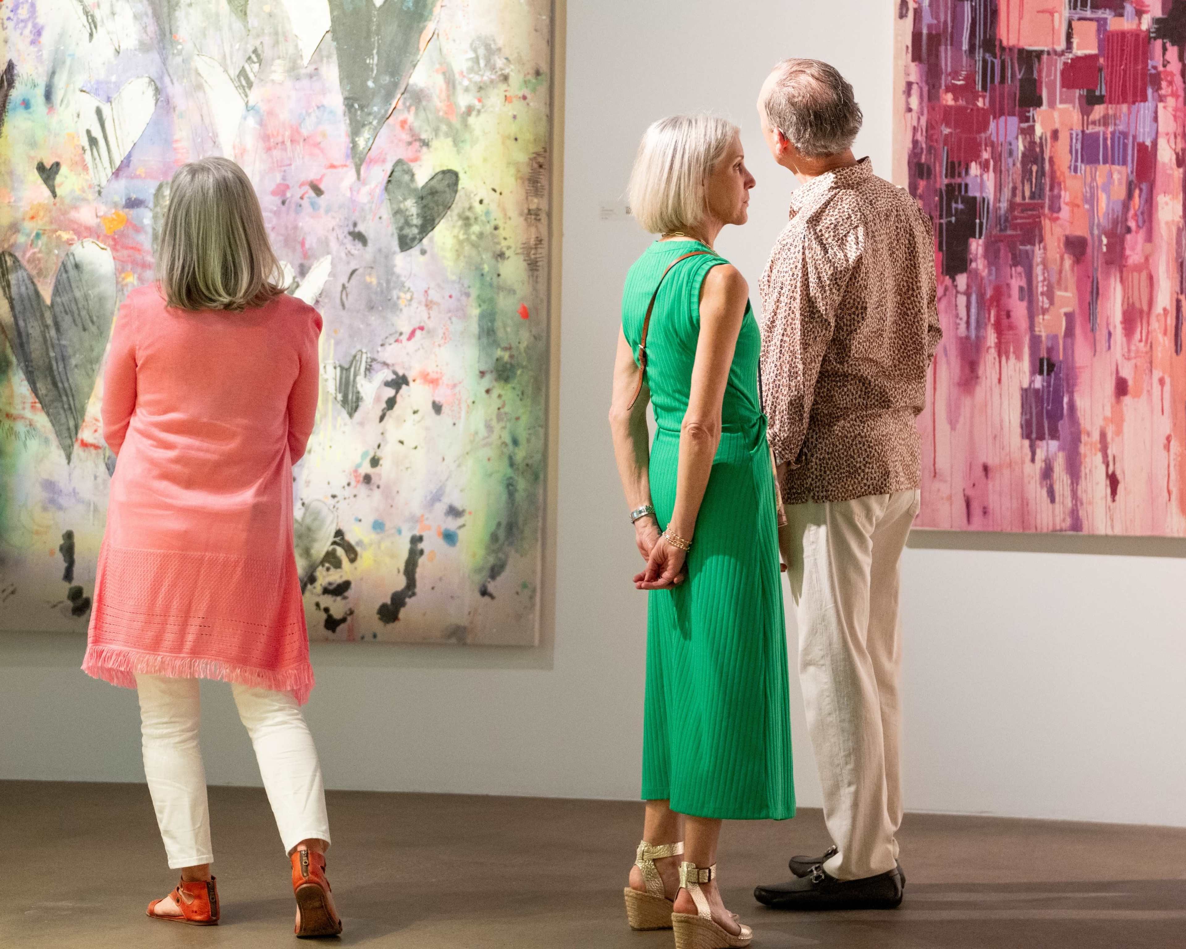 Three people are viewing abstract artworks in an art gallery.