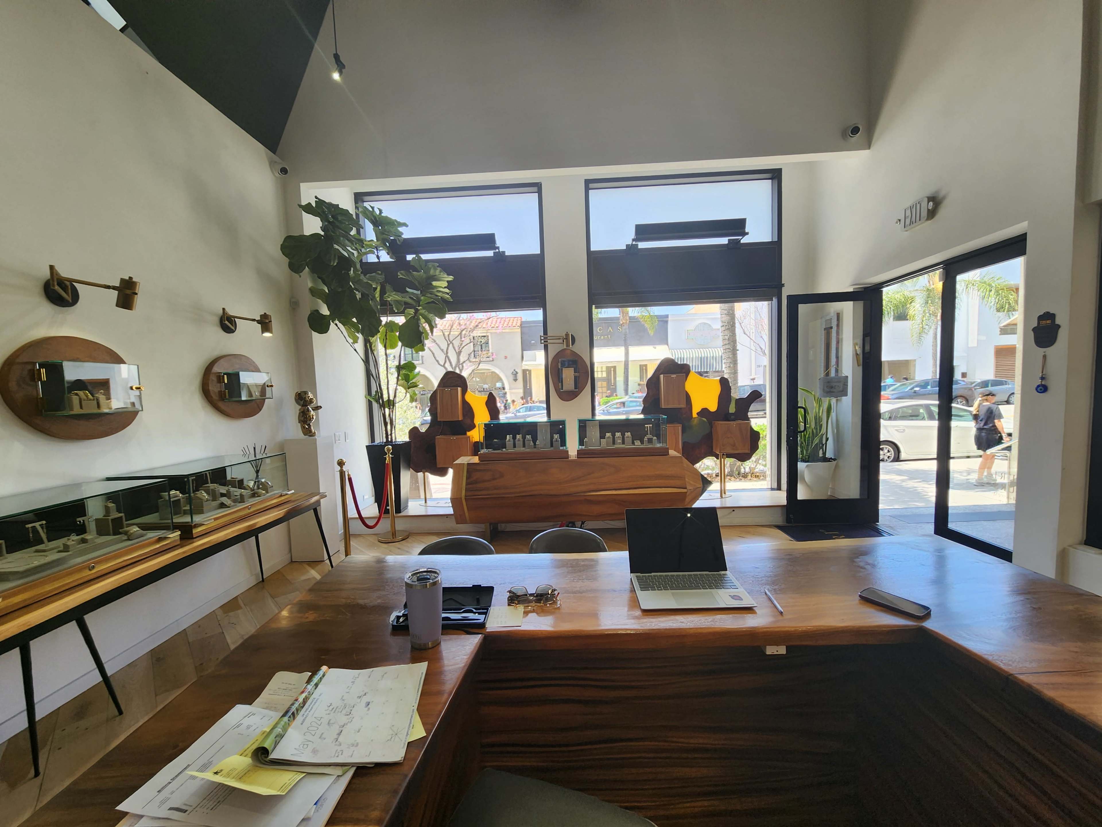 A modern interior of a store features a wooden counter, a laptop on the surface, mirrors on the walls, and large windows facing the street.