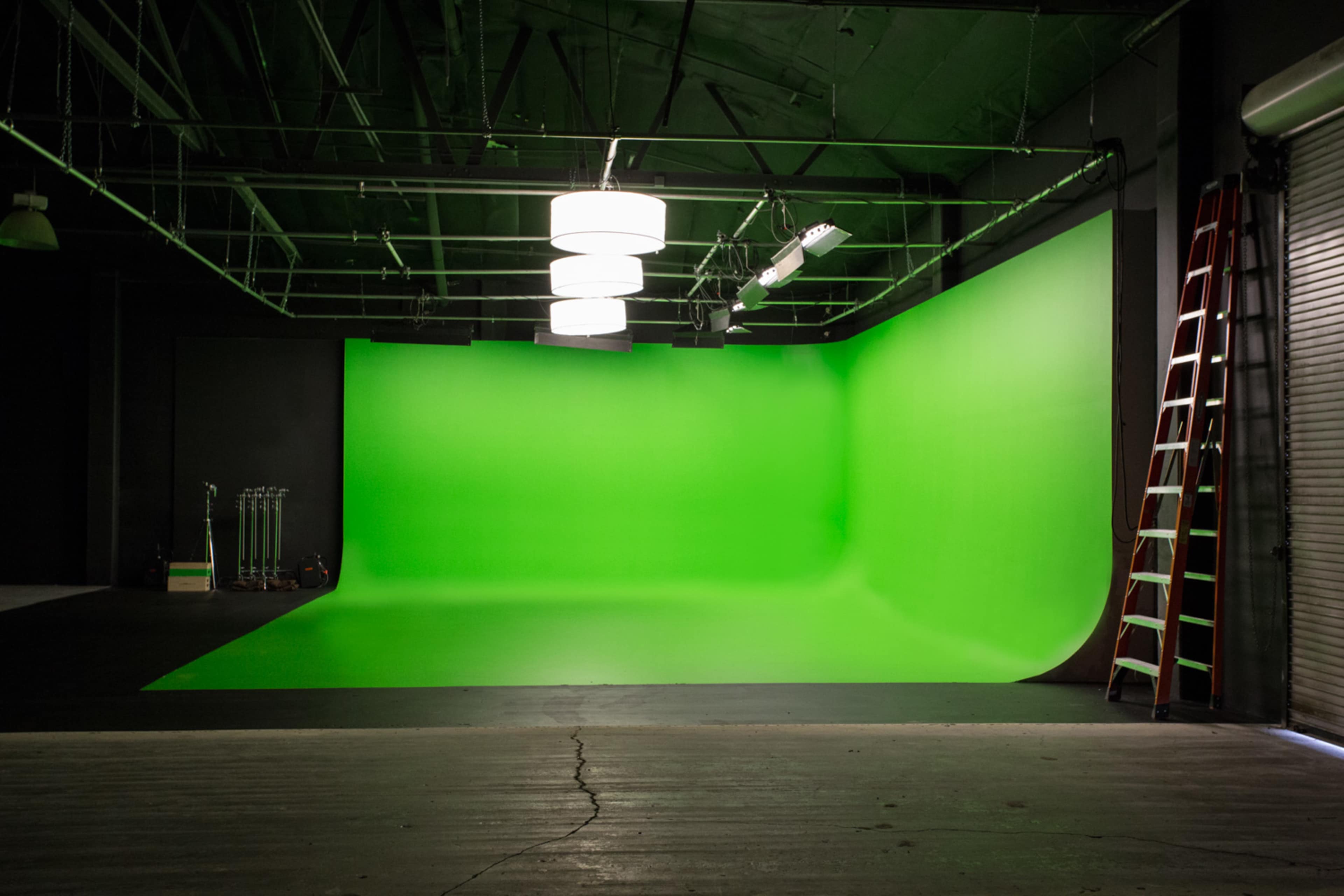 A spacious studio with a large green screen background and a ladder against the wall.