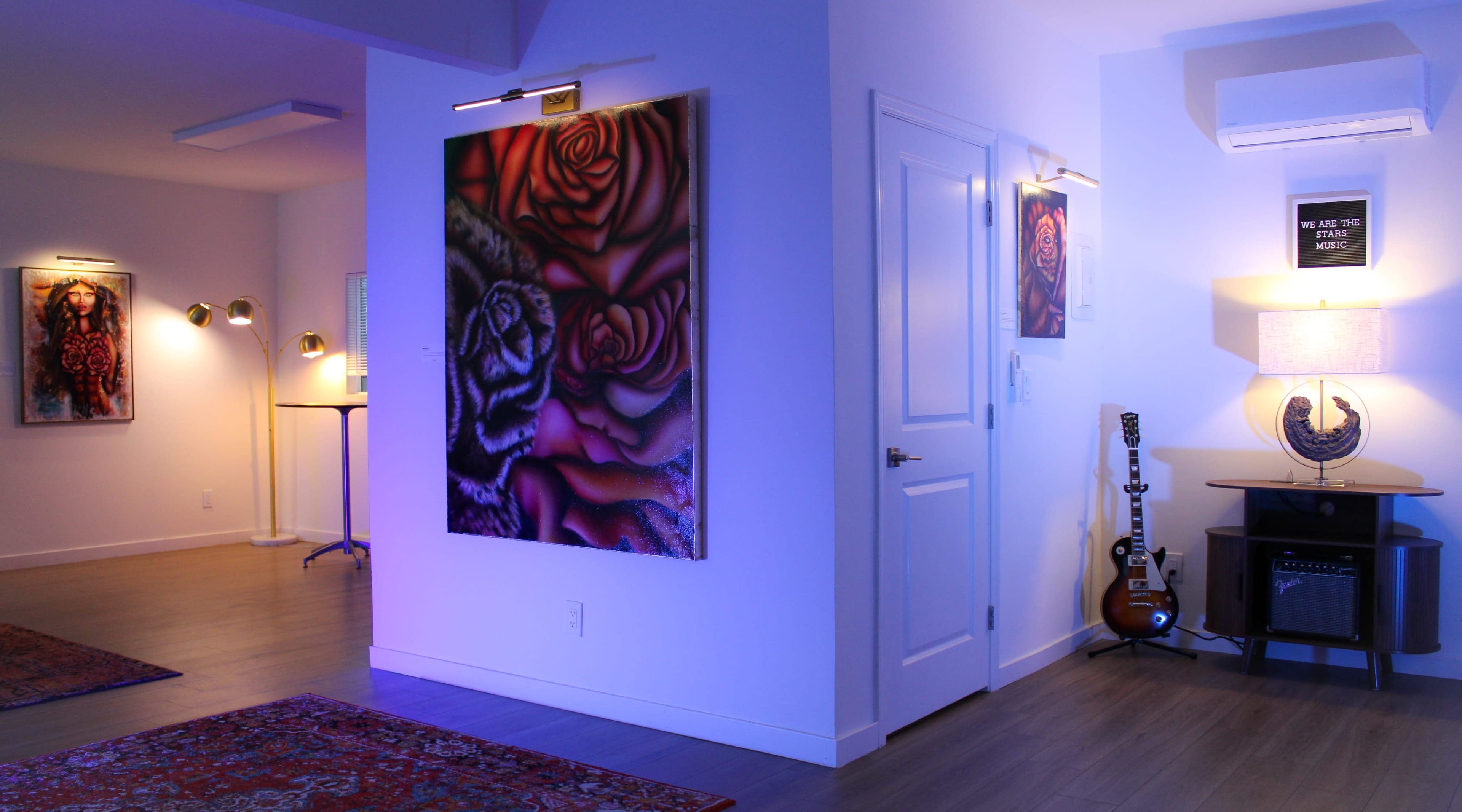 The image shows a brightly lit indoor space featuring colorful wall art, a guitar leaning against an amplifier, and modern lighting fixtures.