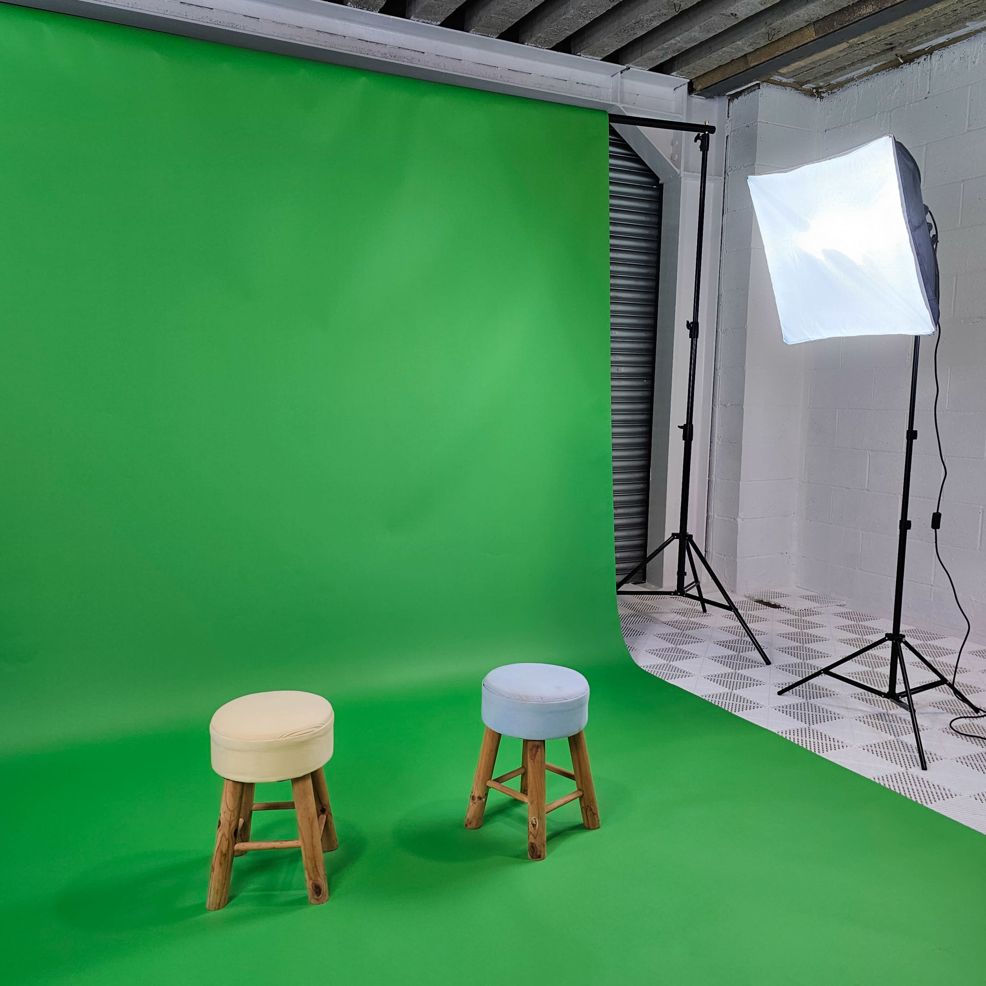 Two stools, one yellow and one light blue, positioned in front of a green backdrop with a softbox light set up to the side.