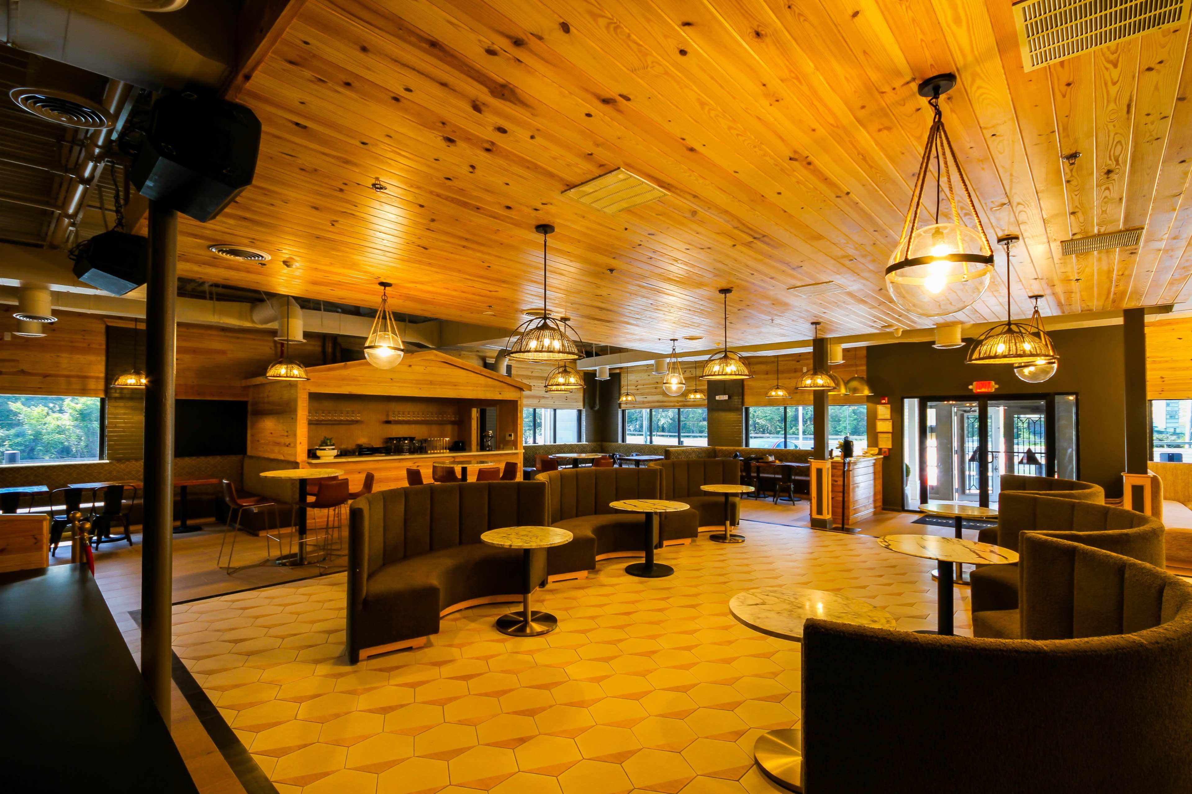 An interior of a restaurant with wooden ceilings, pendant lighting, and a mix of seating areas, including booths and tables.