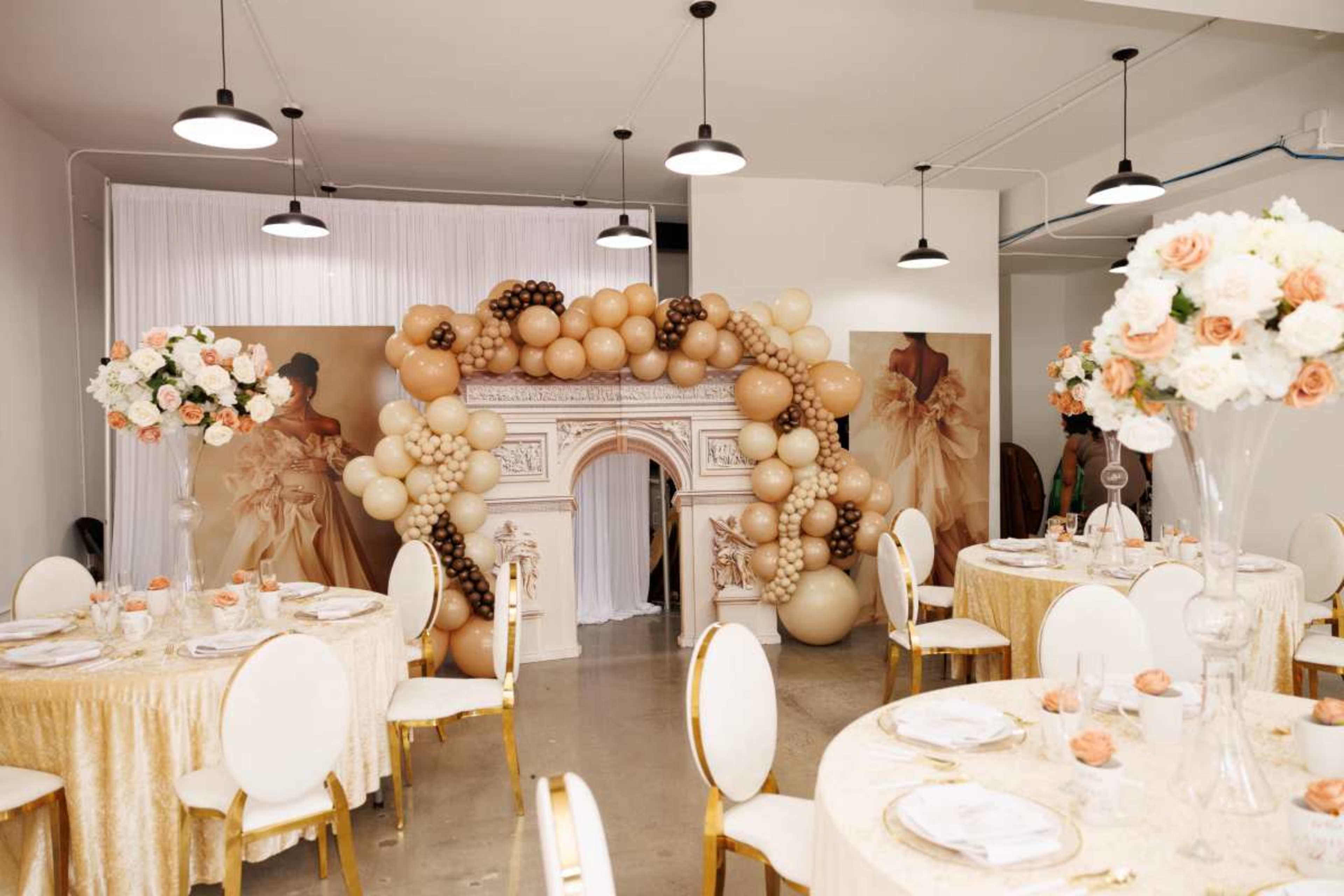 A beautifully decorated event space features elegantly set tables, floral arrangements, and a balloon arch backdrop.