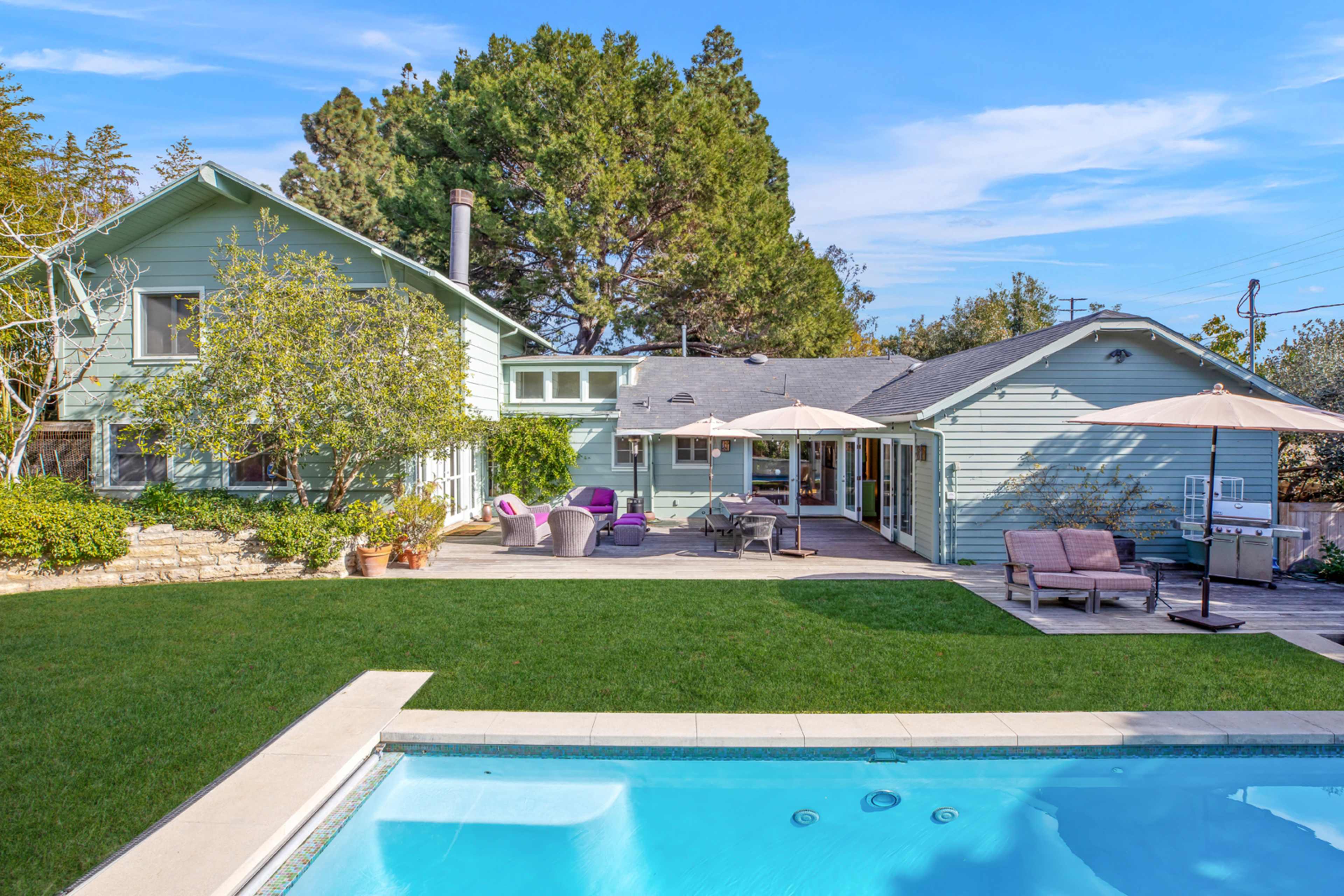 The image features a modern house with light blue siding, a well-maintained lawn, and a swimming pool in the foreground.