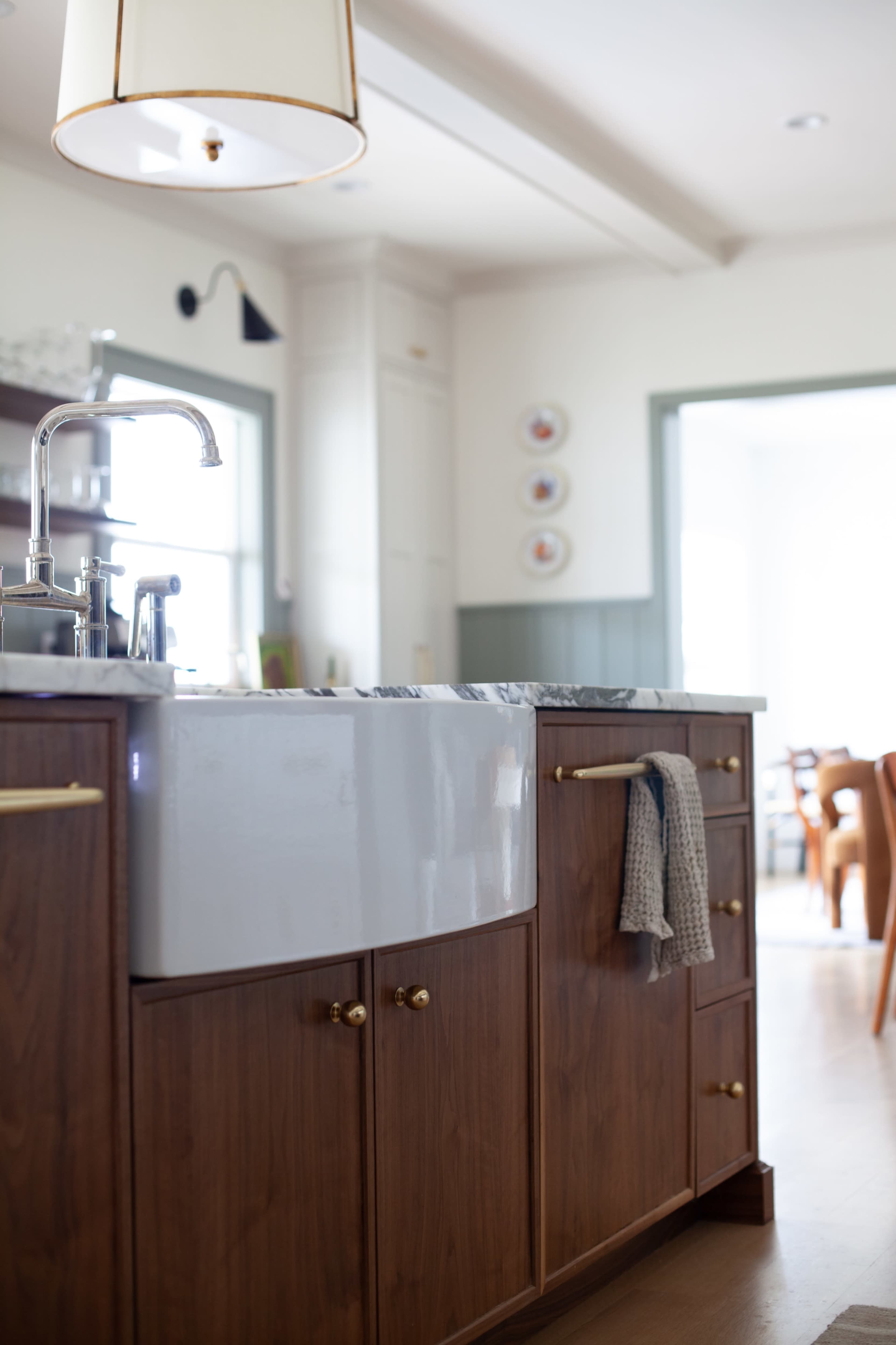 The image shows a kitchen with a farmhouse sink, wooden cabinetry, and a light fixture overhead.