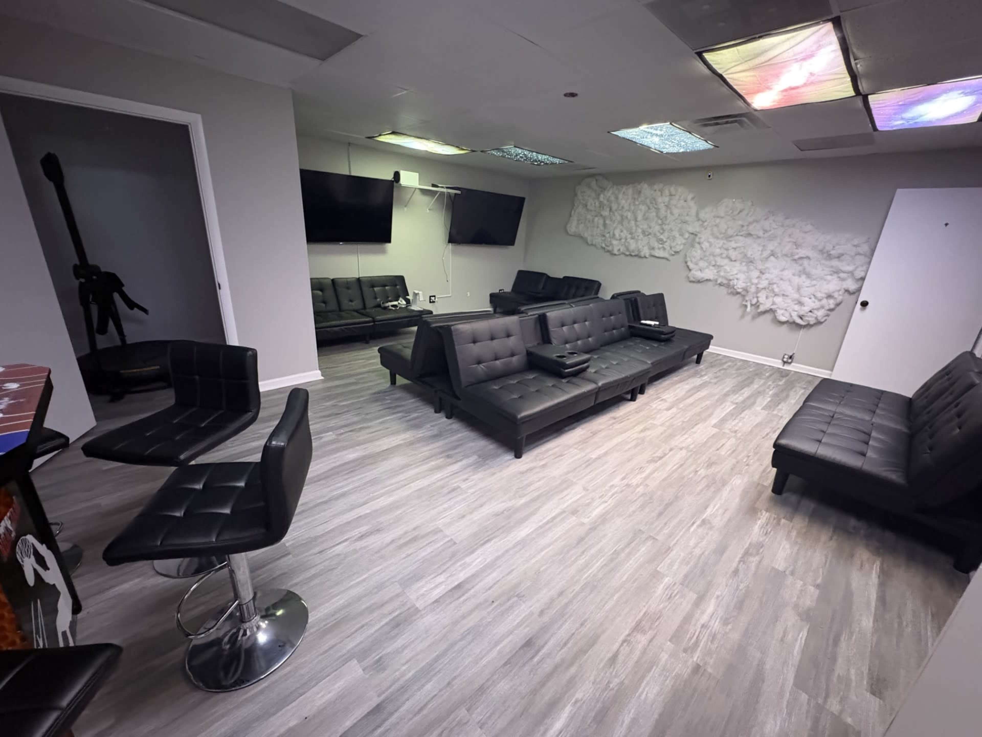The image shows a modern lounge area with black leather furniture, including sofas and chairs, arranged around a light-colored wooden floor.