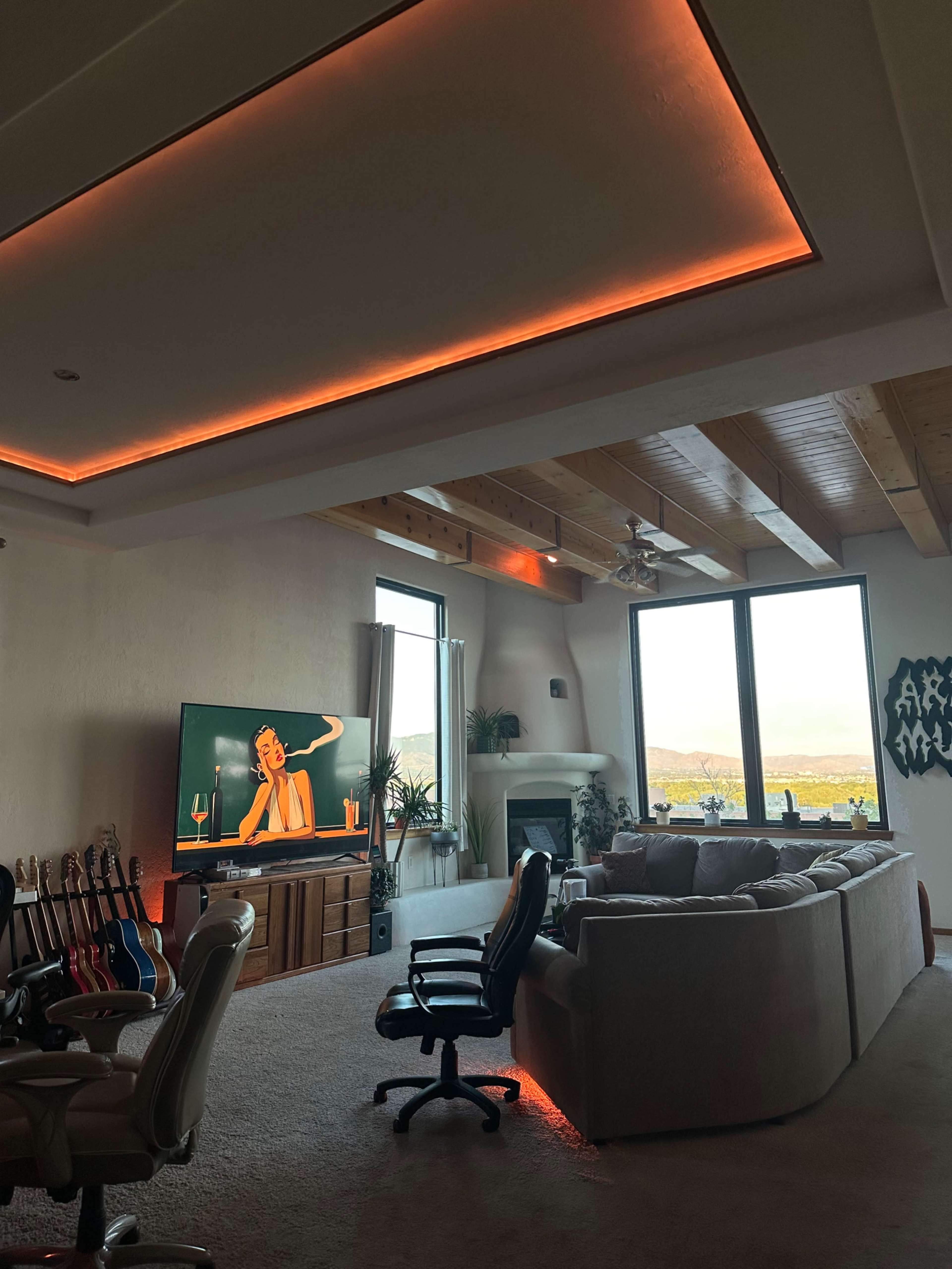 The living room features a large couch, a television displaying an animated character, and large windows with a view.