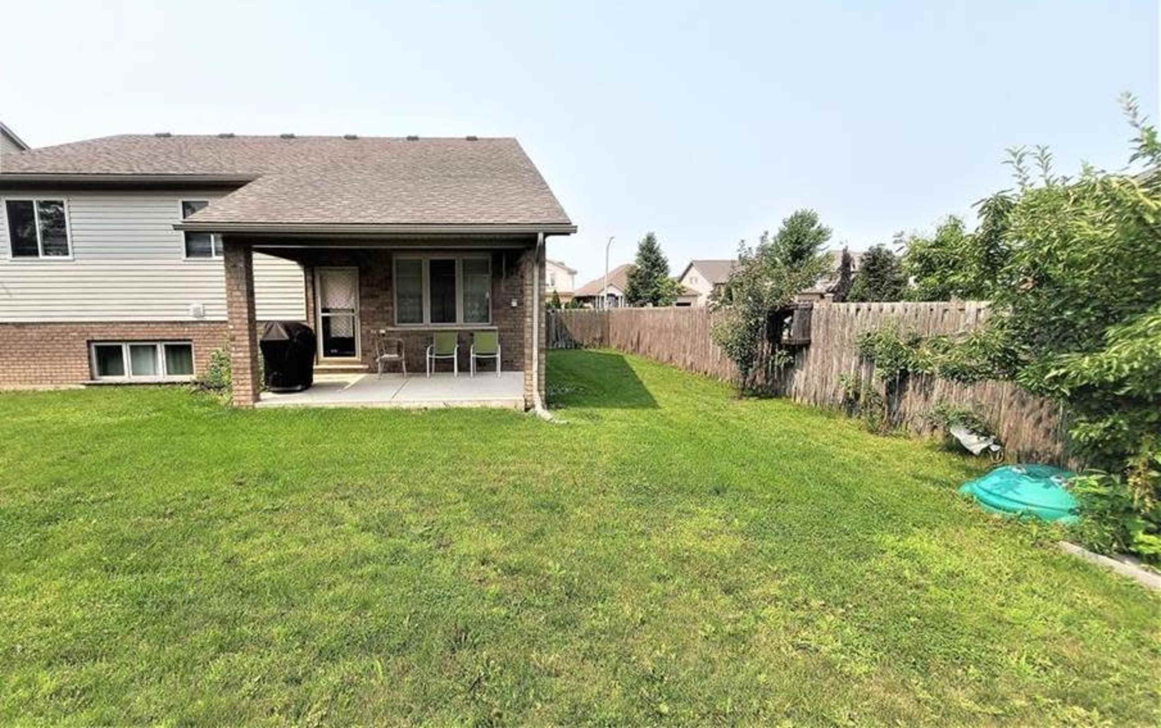 A backyard features a patio area with two chairs, a grill, and a neatly maintained lawn bordered by a wooden fence.
