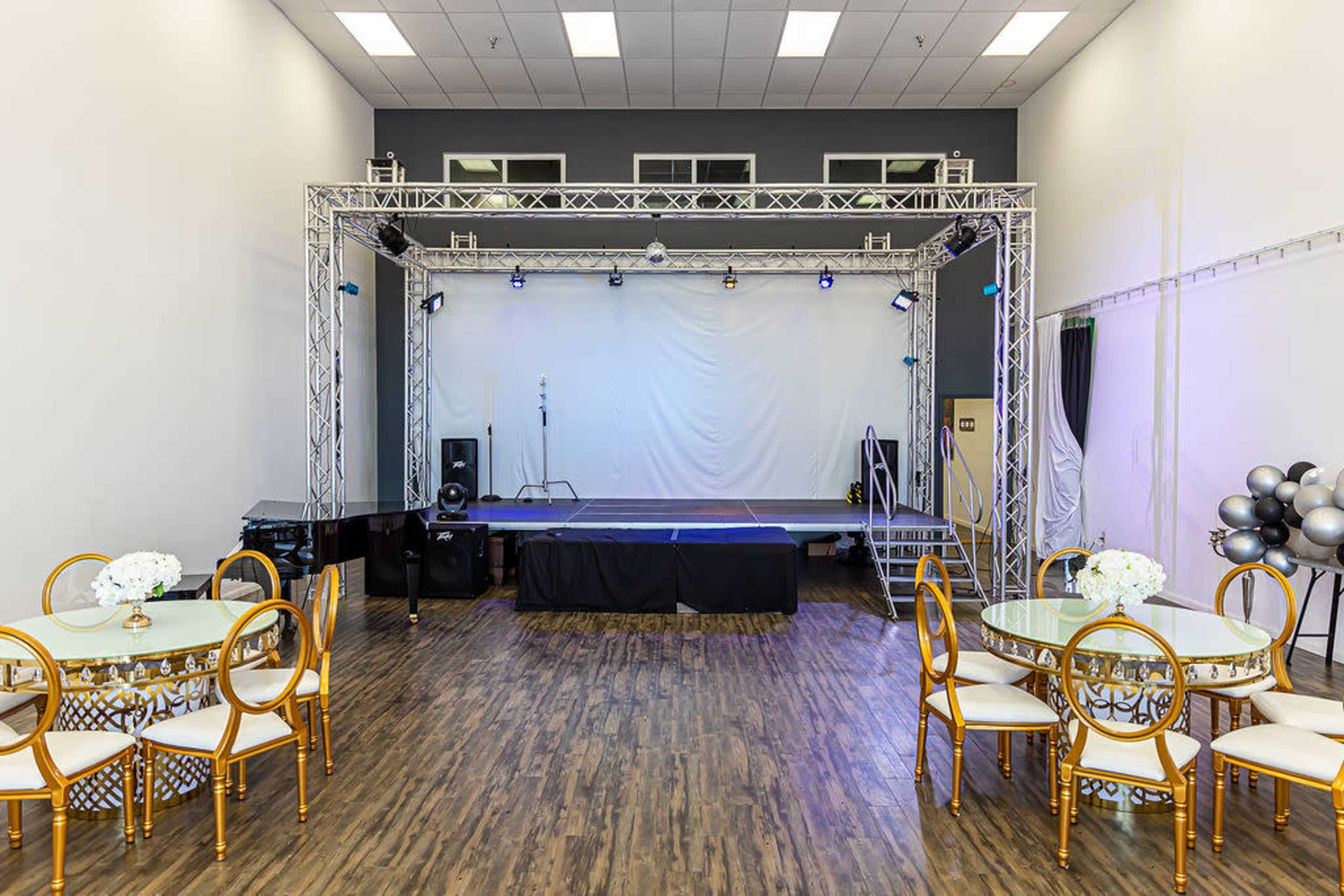 A spacious event venue with a stage at one end and round dining tables set up facing the stage.