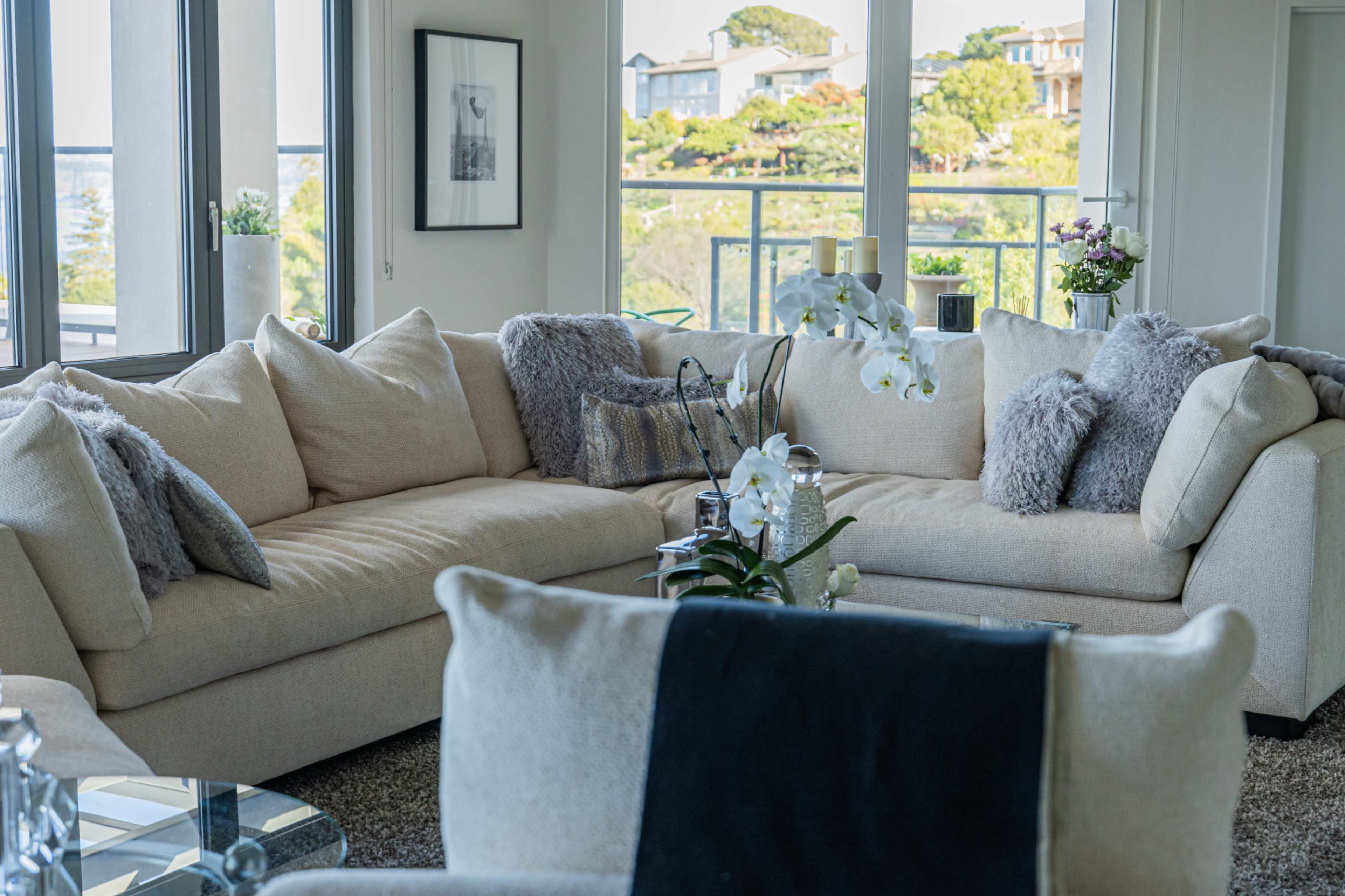 A modern living room with a large L-shaped beige sectional sofa, adorned with decorative pillows and an orchid plant on the coffee table.