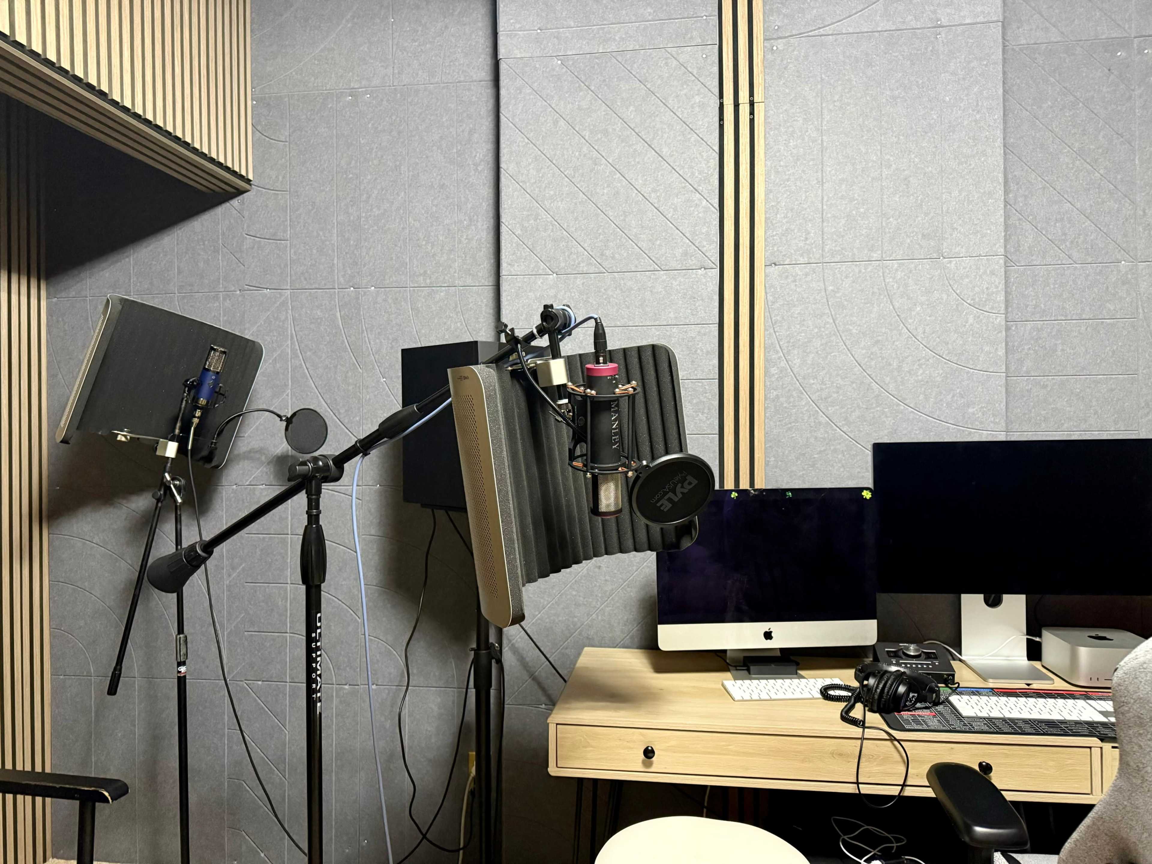 The image shows a sound recording studio setup with microphones mounted on stands next to computer monitors and a desk.