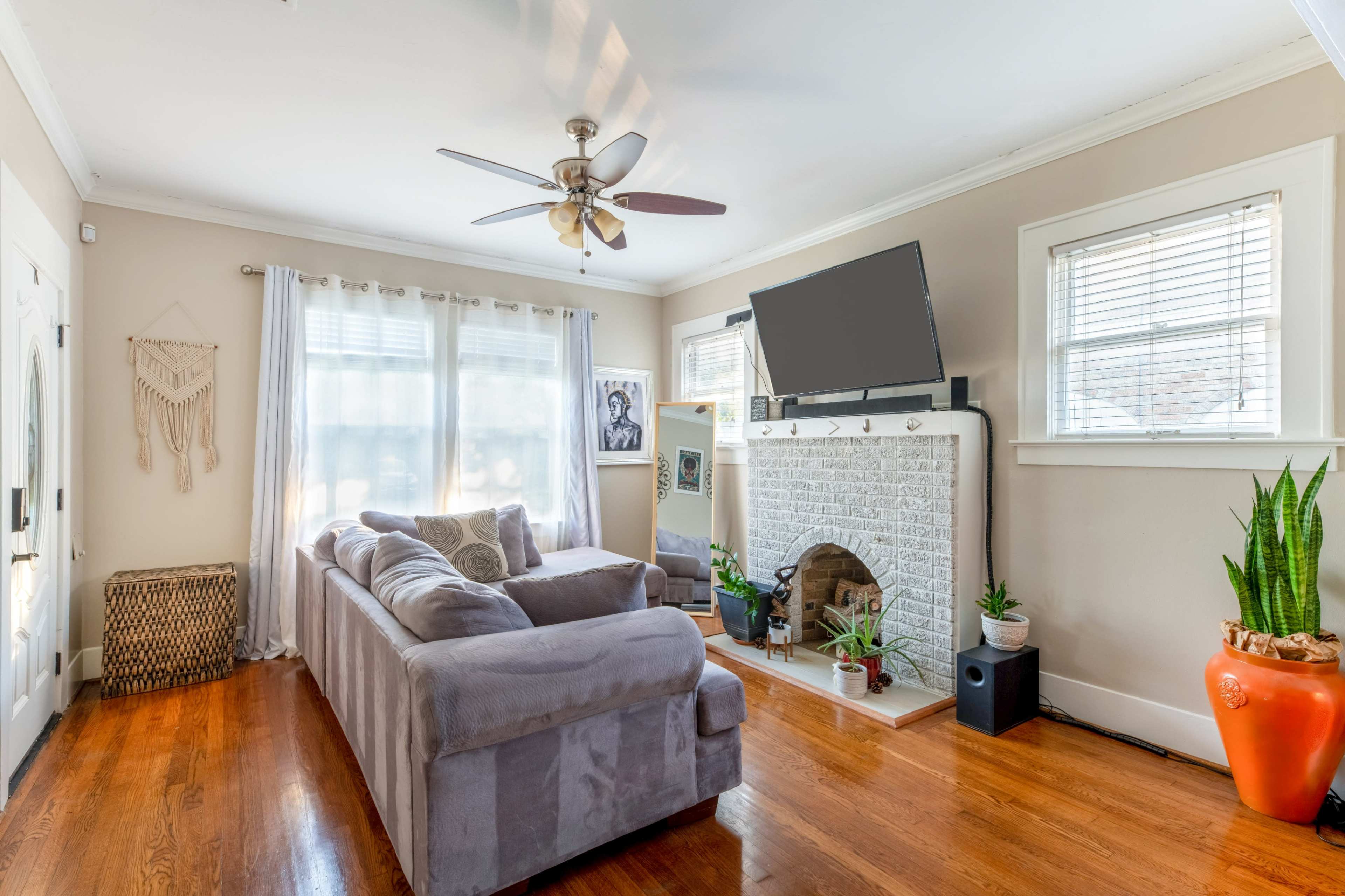 A cozy living room features a sectional couch, a stone fireplace with a television above it, and large windows with natural light.