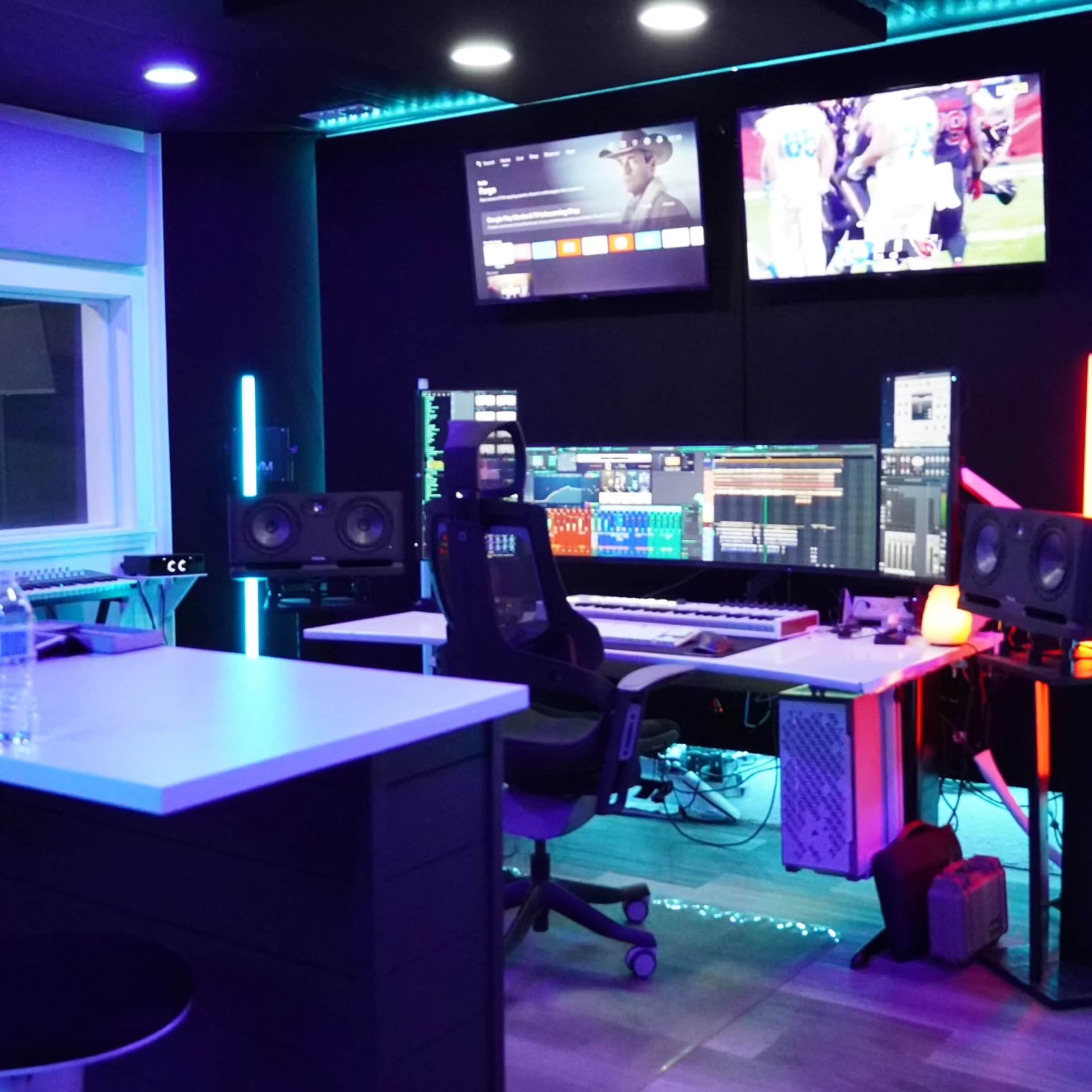A modern music production studio with multiple screens, a keyboard, speakers, and colorful LED lighting.