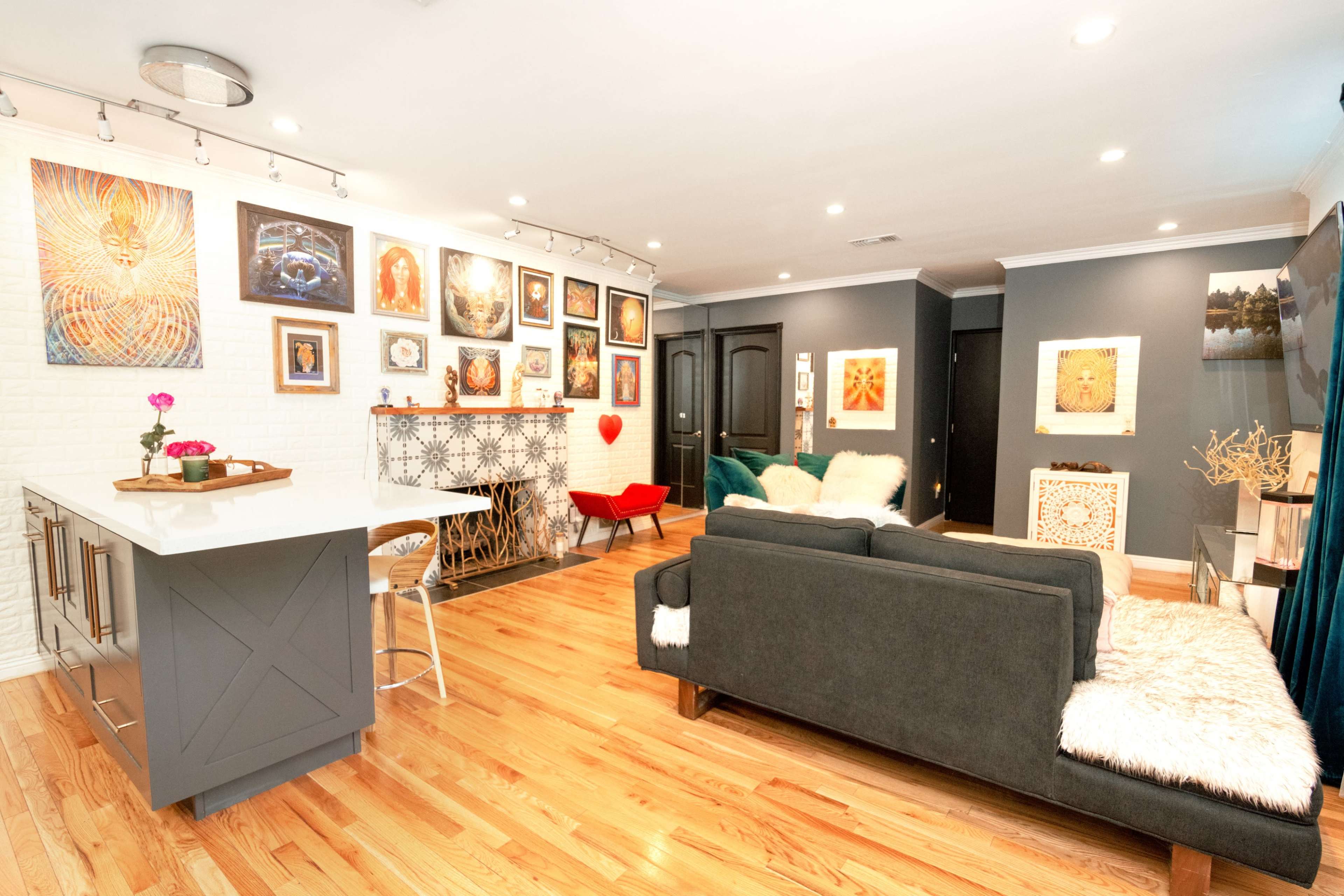 A modern living room features a minimalist sofa, a decorative fireplace, and an arrangement of colorful artwork on the walls.