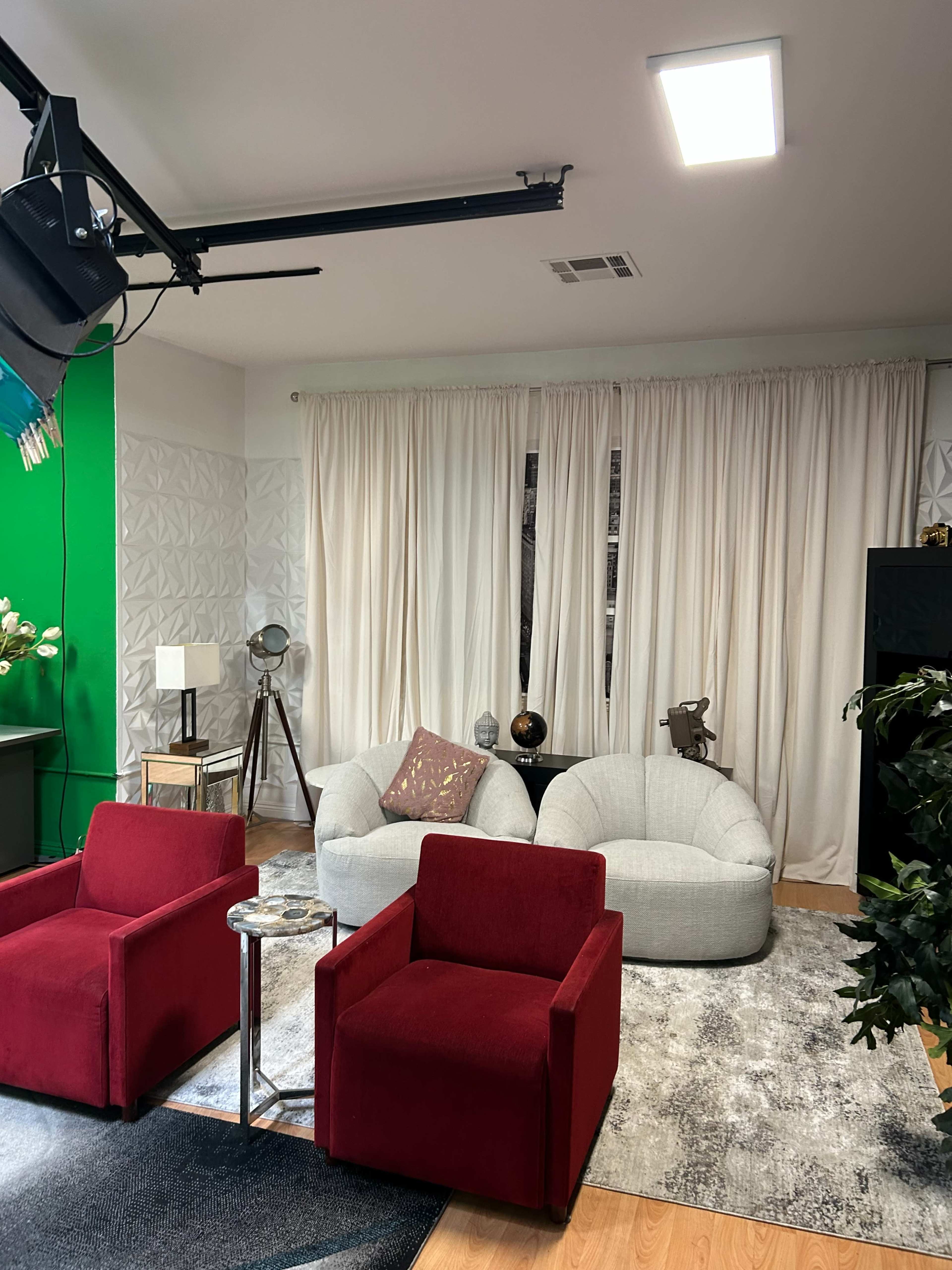 The image shows a modern living space featuring two red armchairs, a gray bean bag chair, a small round table, and a textured area rug, with green and white walls in the background.