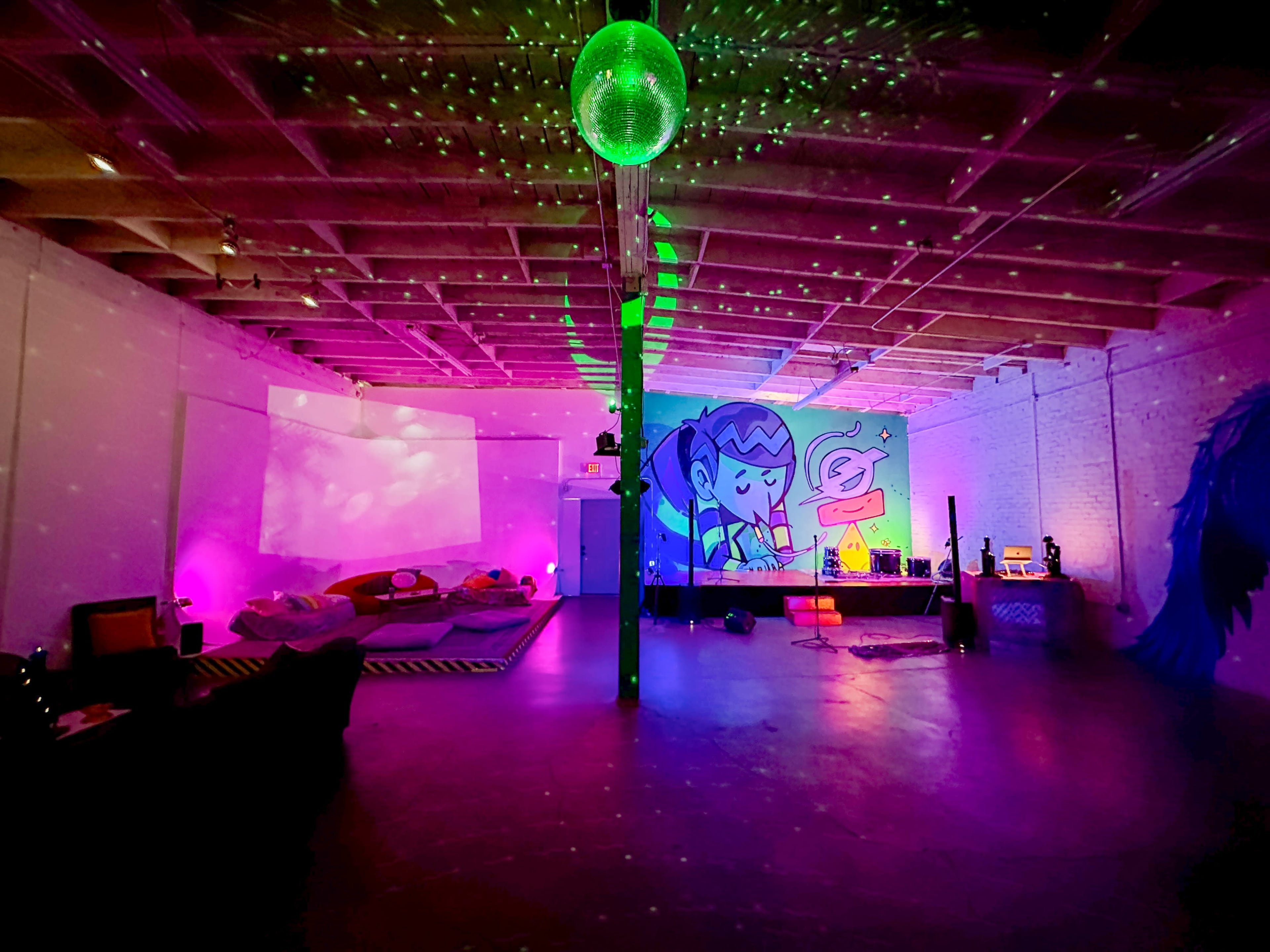 A vibrant, open room with colorful lighting, a disco ball, and a mural of a character on one wall.