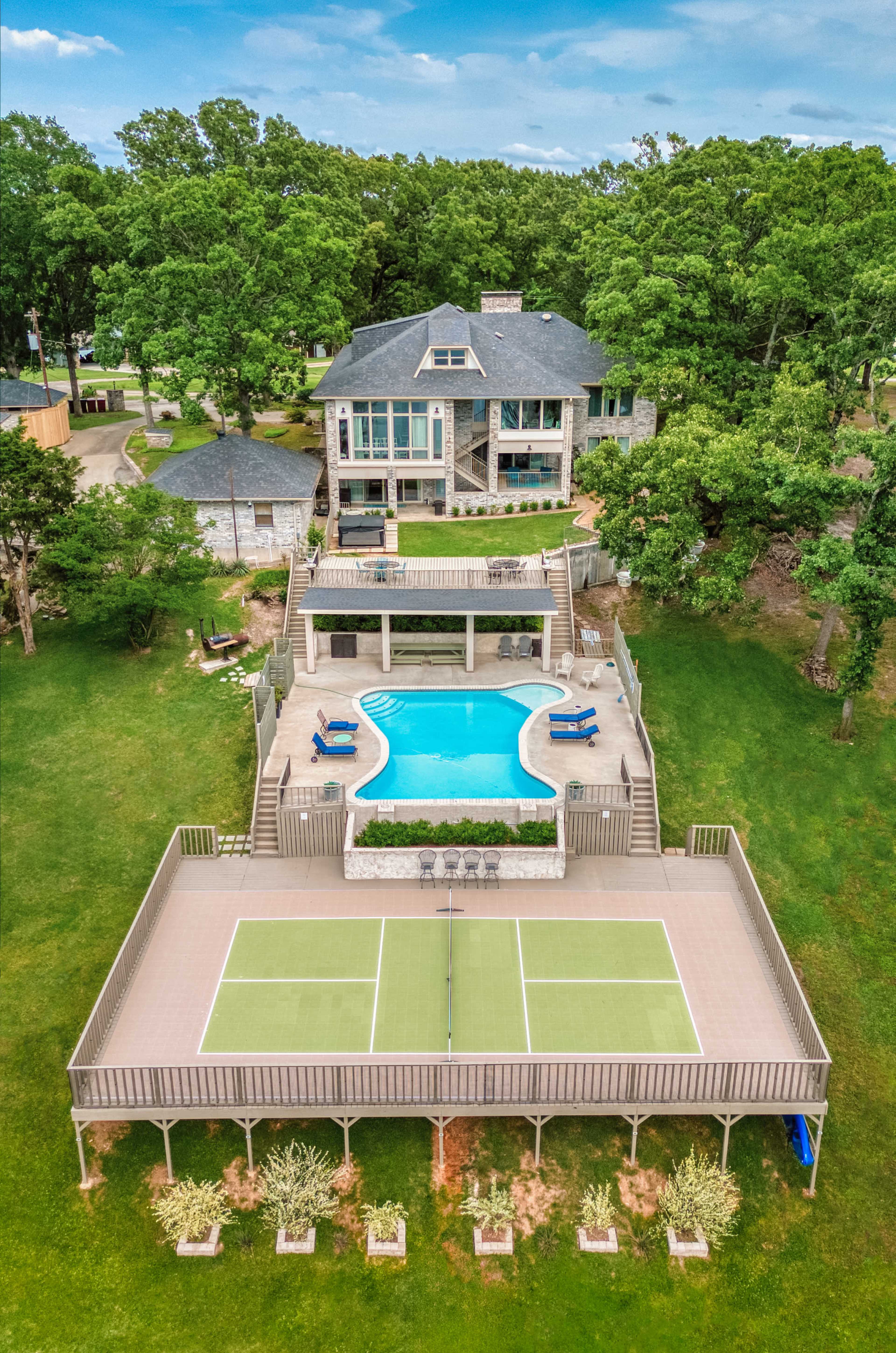 The image shows a large house with a swimming pool and tennis court situated in a green landscape.