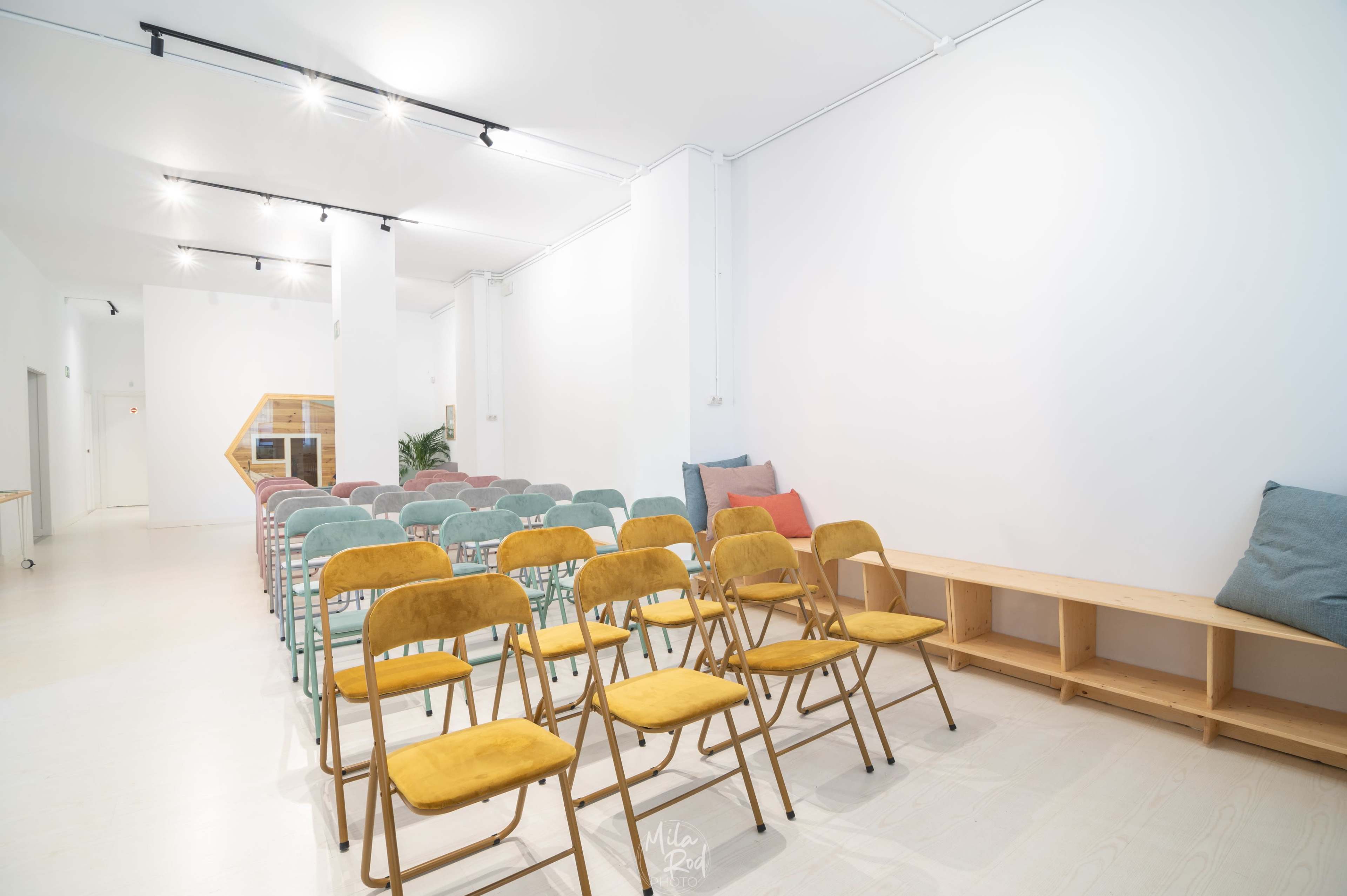 A spacious room set up for an event with rows of colored chairs and a wooden bench.